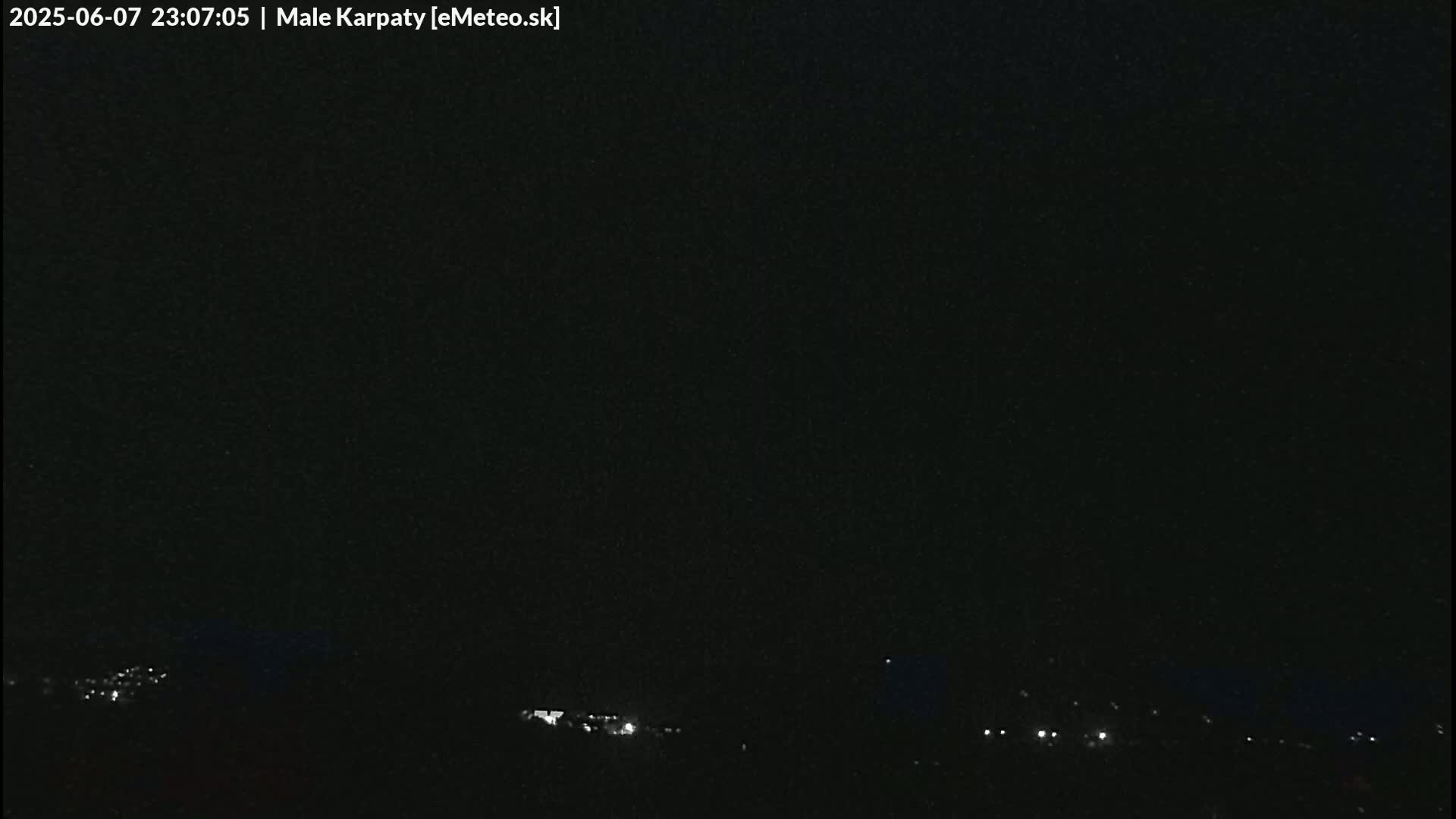 A nighttime, dark view shows a few distant lights on the horizon under a clear, black sky.