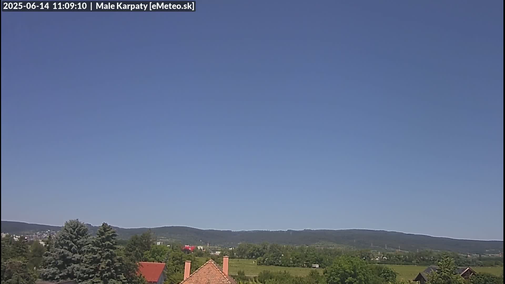 A clear blue sky overlooks a landscape of green trees, fields, and distant mountains.