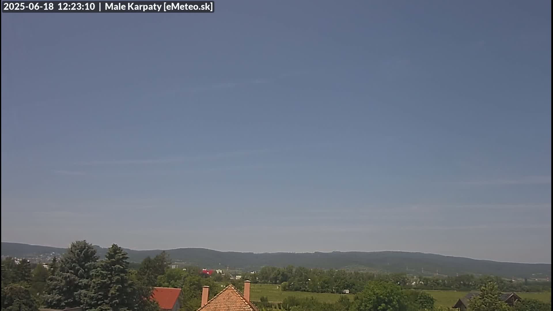 A mostly clear sky overlooks a landscape of green trees, fields, and distant hills under a light blue sky.