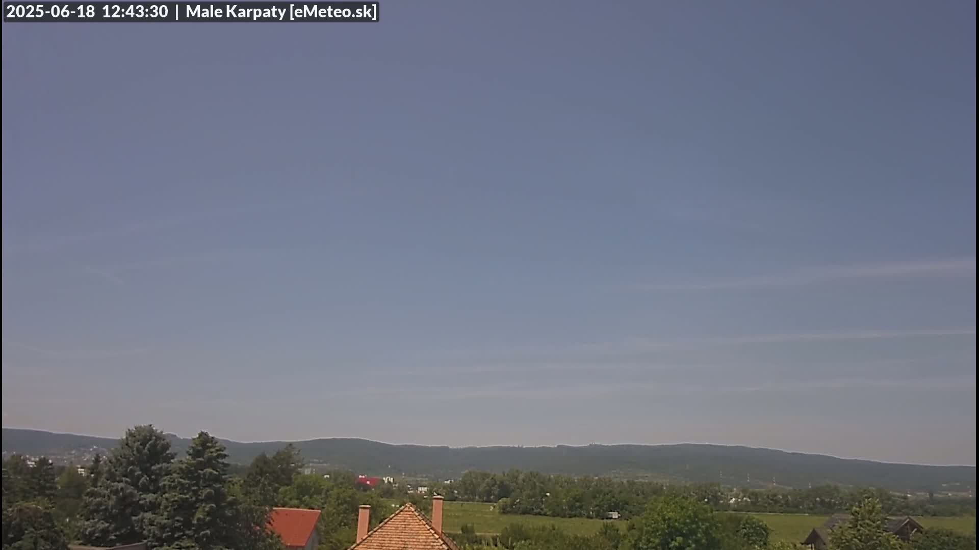 A clear, light-blue sky over a landscape of green trees, fields, and distant mountains.