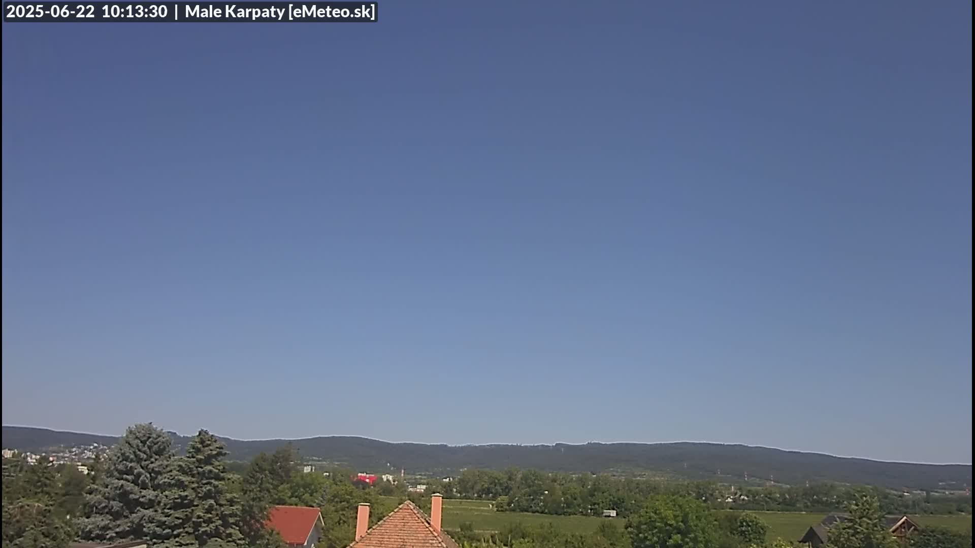 A clear blue sky overlooks a landscape of green trees, fields, and distant mountains.