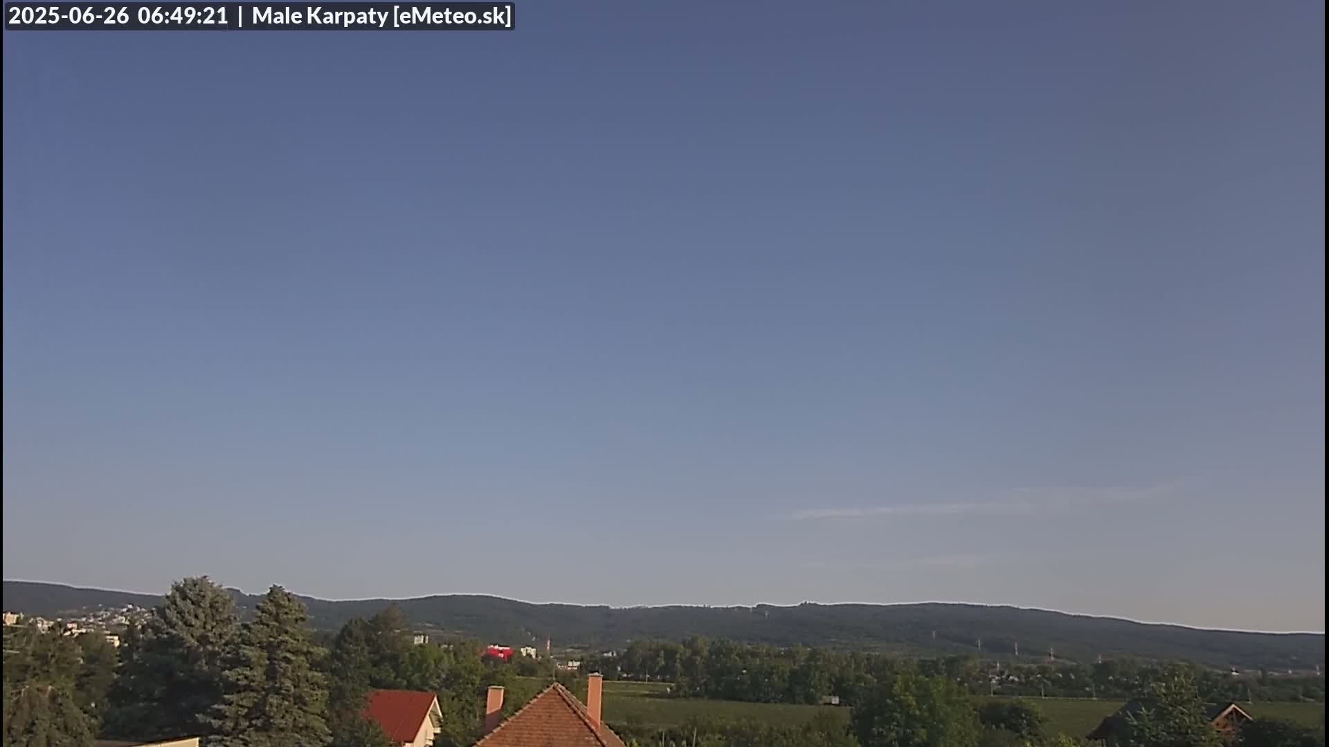 A mostly clear blue sky with wispy, white clouds stretches over a distant mountain range and a tree-lined landscape.