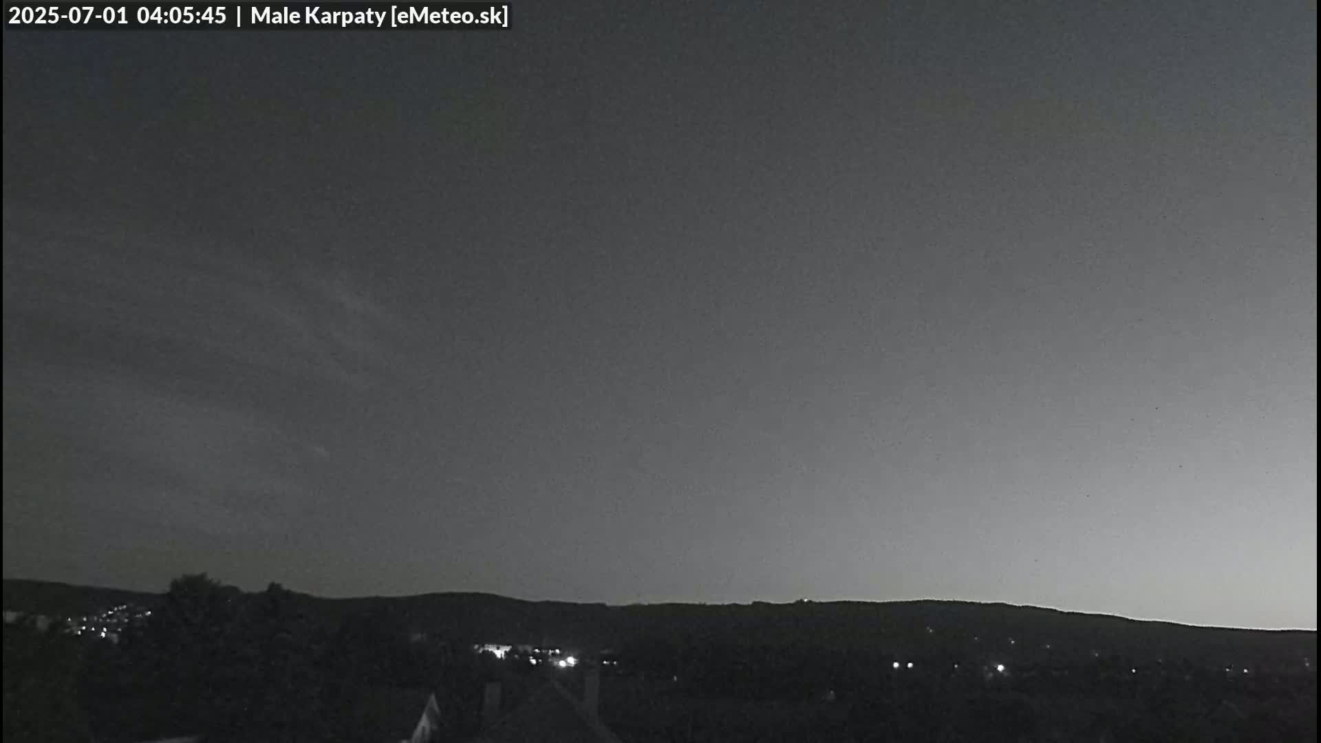 A dark, mostly clear night sky is over a hilly landscape with a few lights visible in the distance.