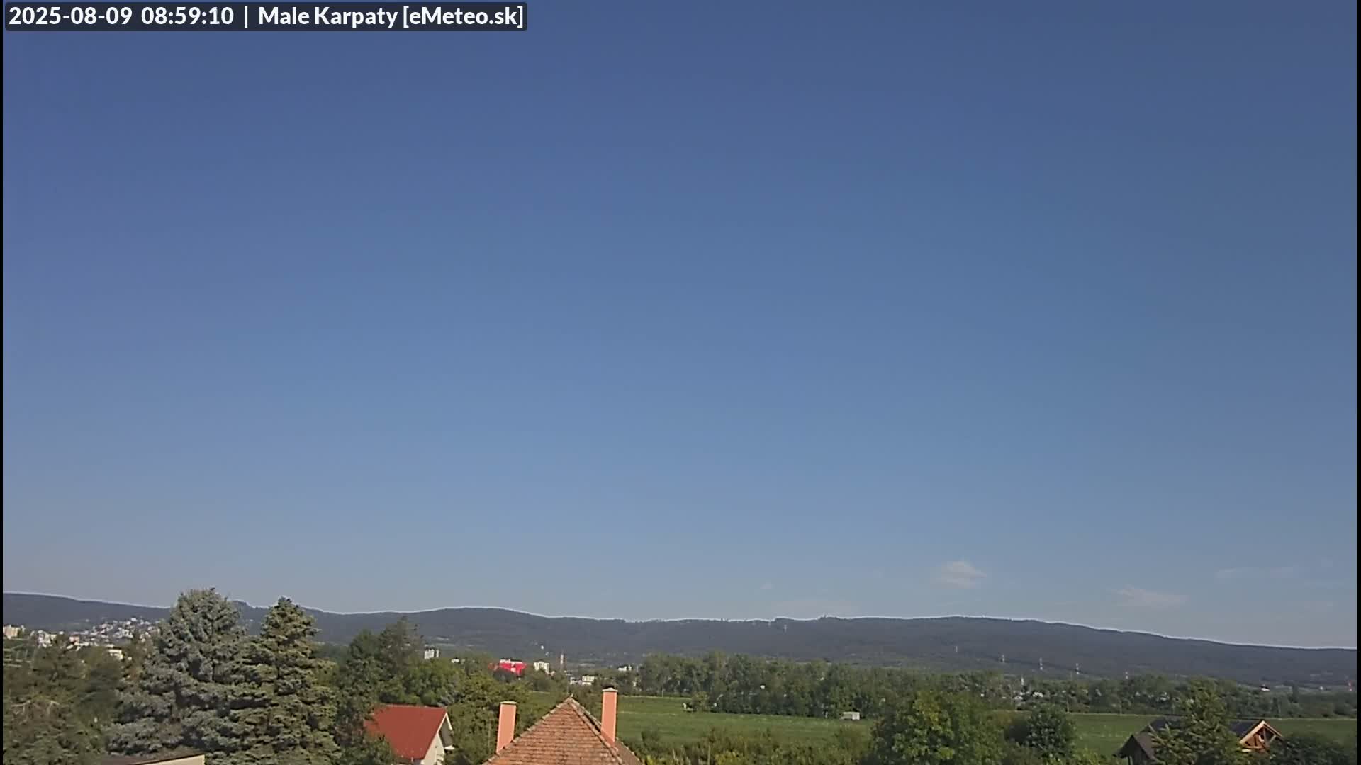 A clear blue sky overlooks a landscape of houses, trees, and distant mountains.