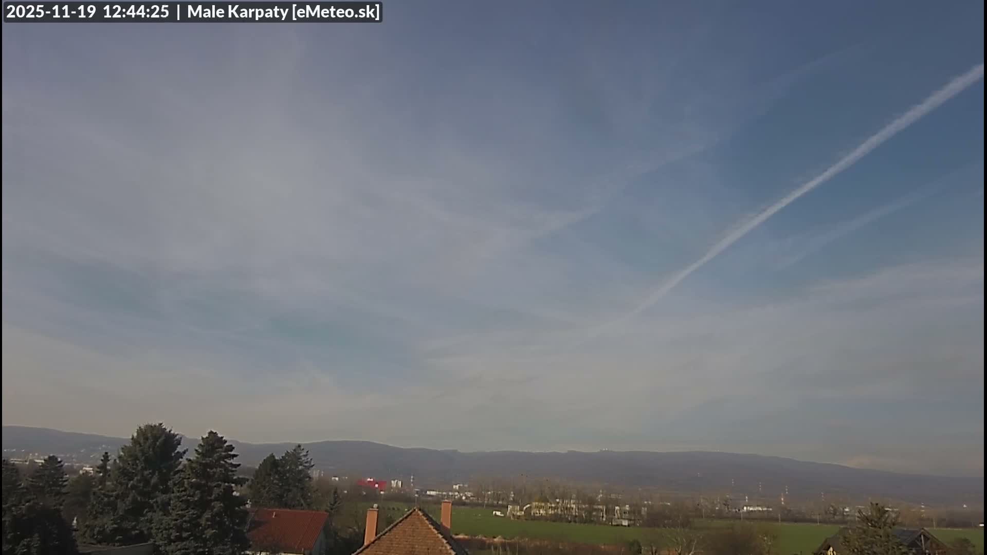 A clear blue sky overlooks a landscape of houses, trees, and distant mountains.