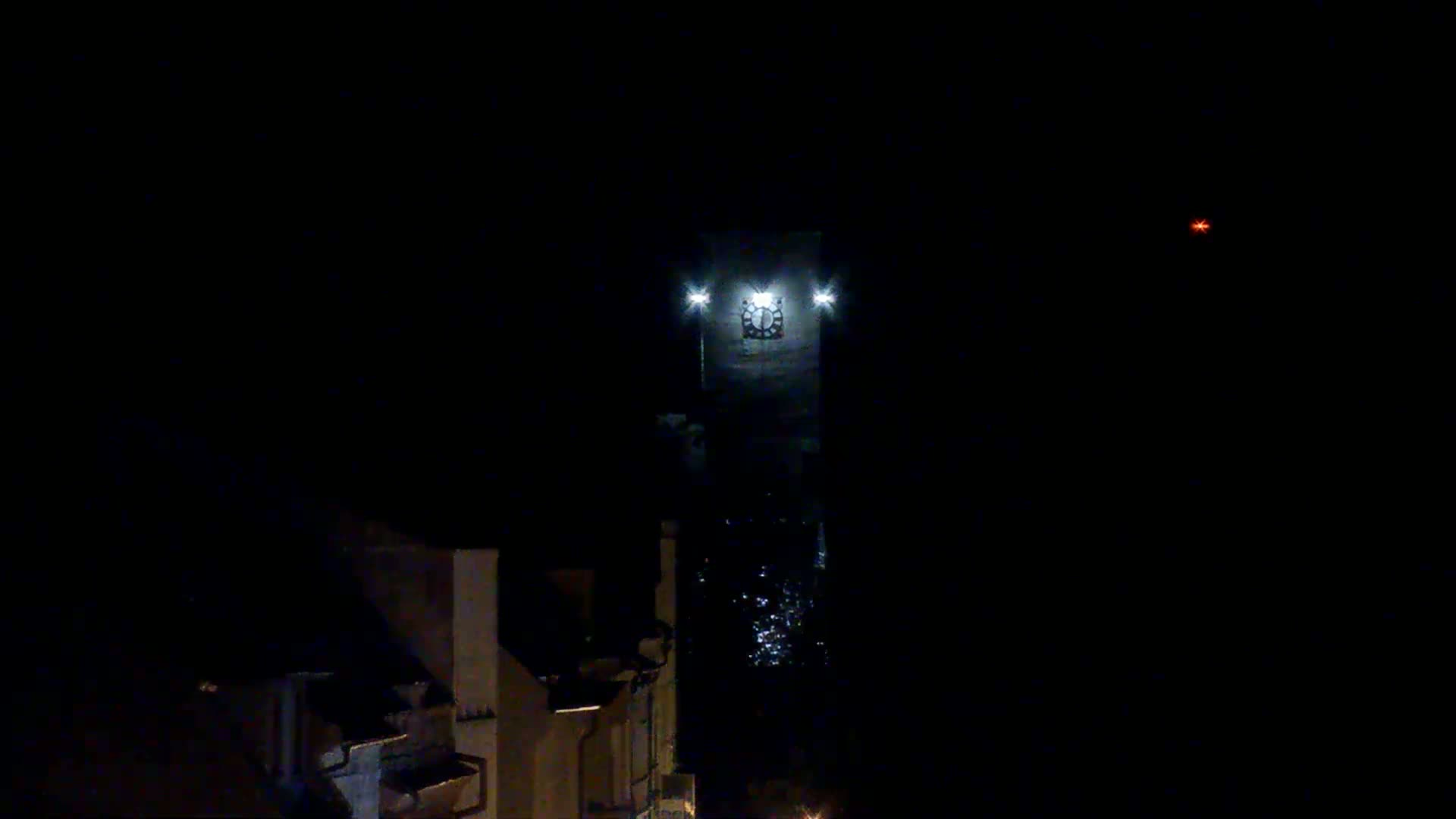A brightly lit clock tower stands tall against a dark night sky, with a faint reddish light visible in the distance.