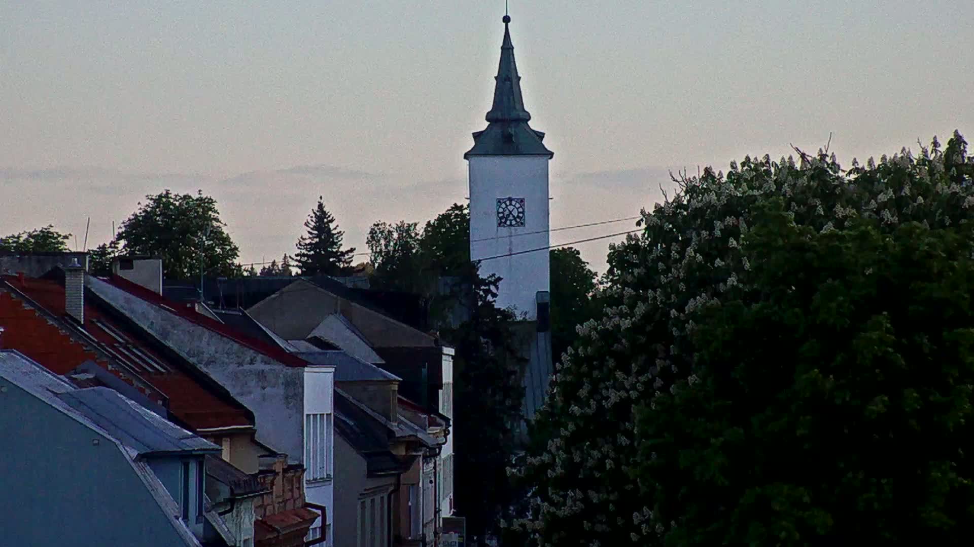 A tall, white clock tower rises above a row of houses under a hazy, overcast sky.