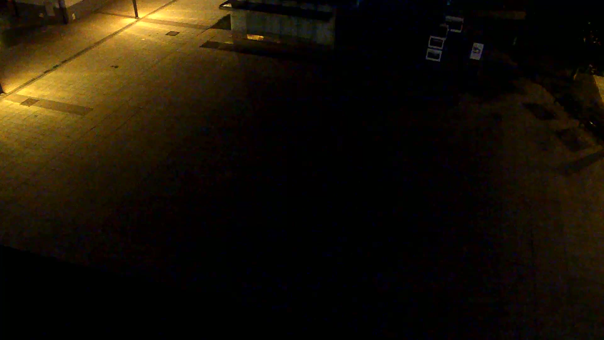 A dark, paved plaza is dimly lit by several streetlights at night.