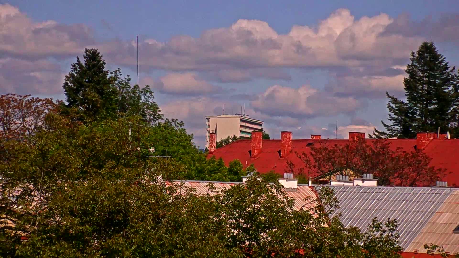 Red-roofed buildings and green trees are visible under a partly cloudy sky.