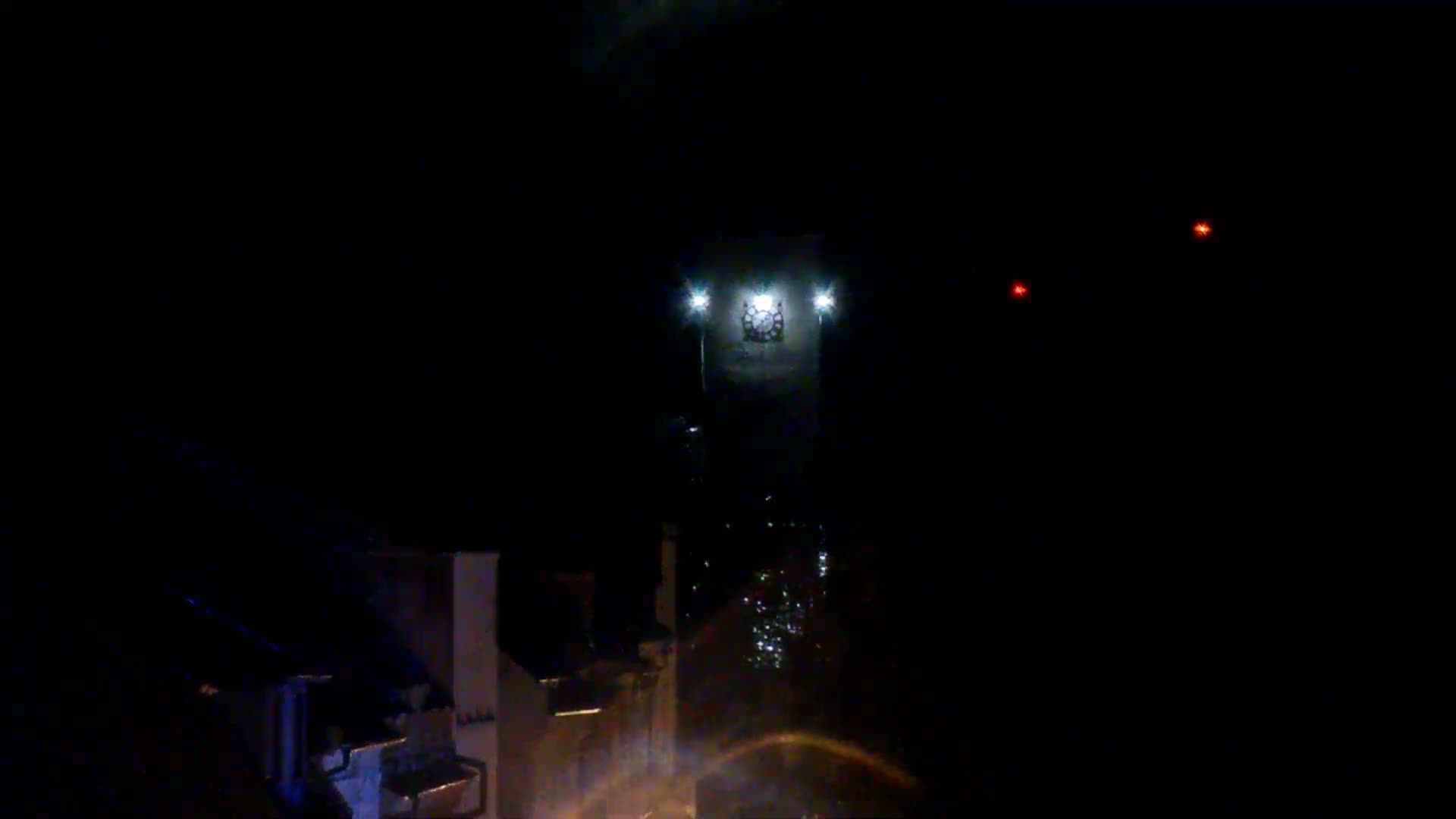 A nighttime view shows a brightly lit object in the distance, possibly a building, with two faint red lights visible to the right.