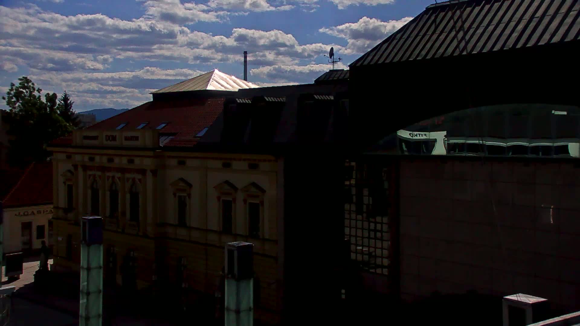 A partly sunny day shows a view of several buildings, including a tan building with many windows and a darker, modern building with a large window reflecting a lighter building.