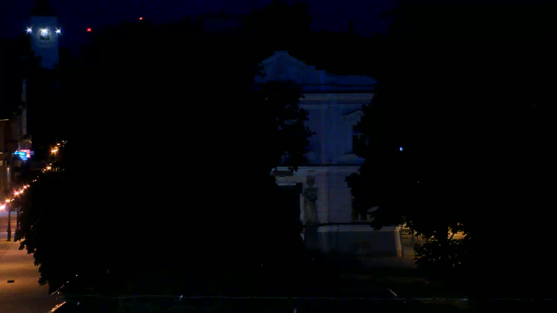 A dimly lit nighttime street scene shows a partially visible building with a statue, trees, and streetlights.