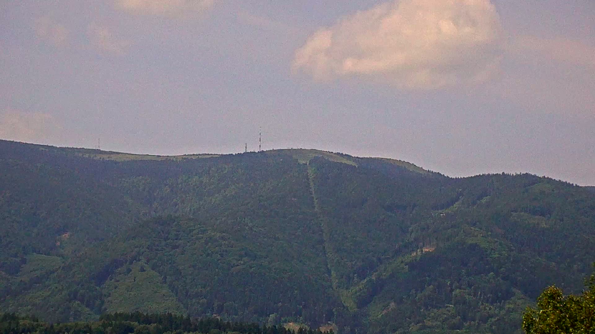 A distant, tree-covered mountain range with communication towers on a peak under a partly cloudy sky.