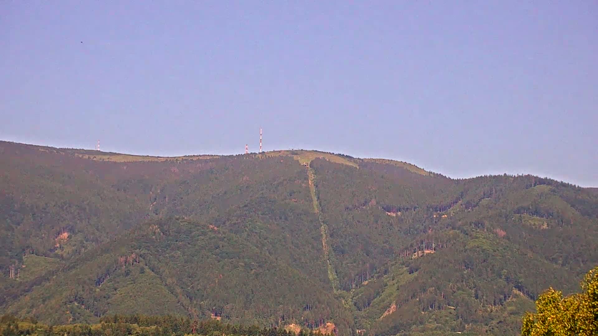 A distant, forested mountain with a tall communication tower on its peak under a clear, light-blue sky.