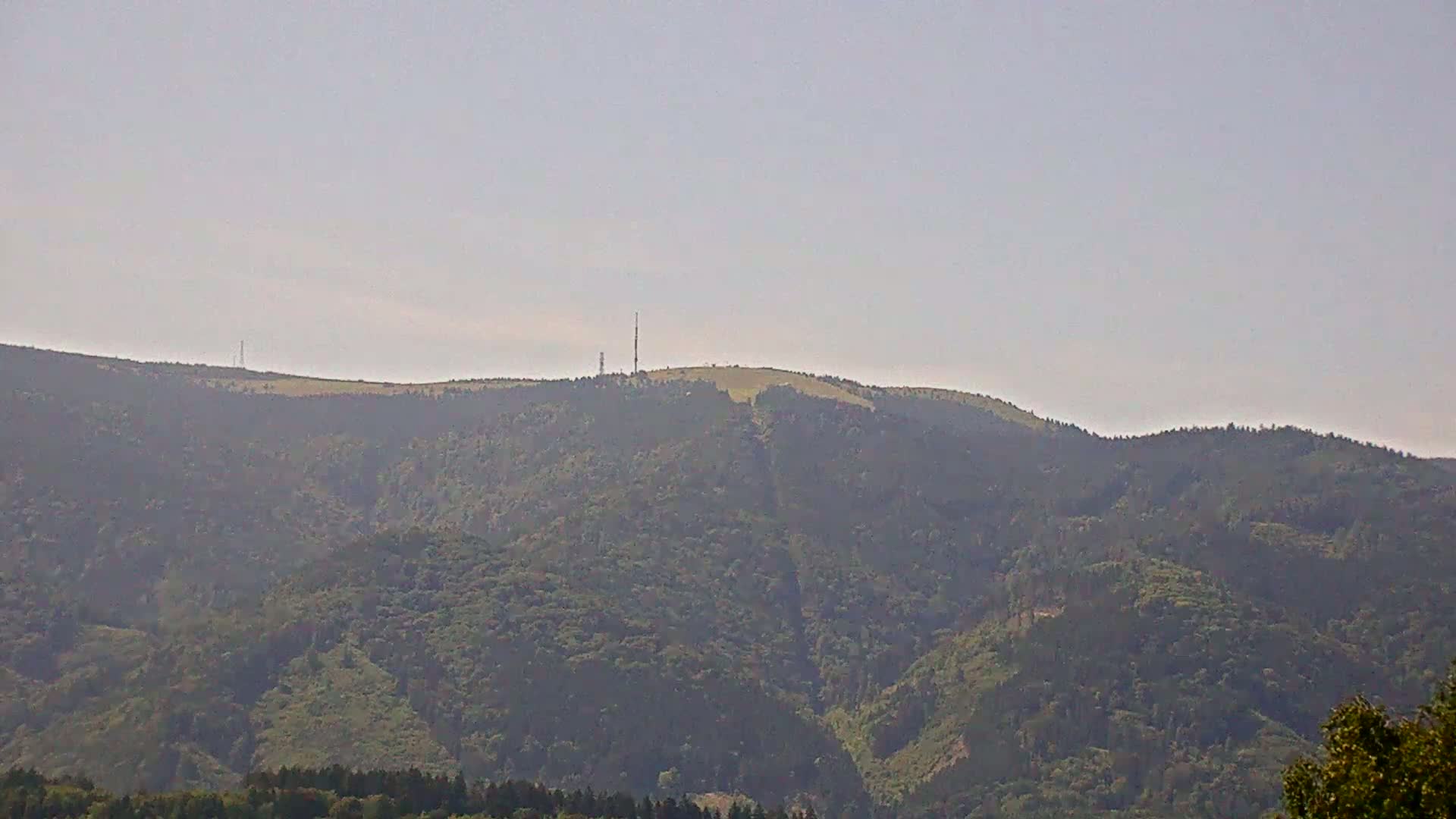 A hazy view of a tree-covered mountain range with two communication towers atop a hill in the distance.