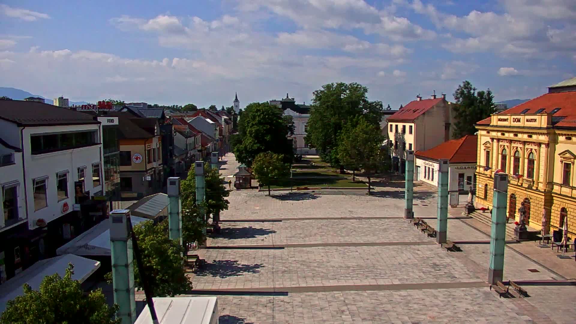 A large town square with several buildings surrounding it, under a partly cloudy sky.