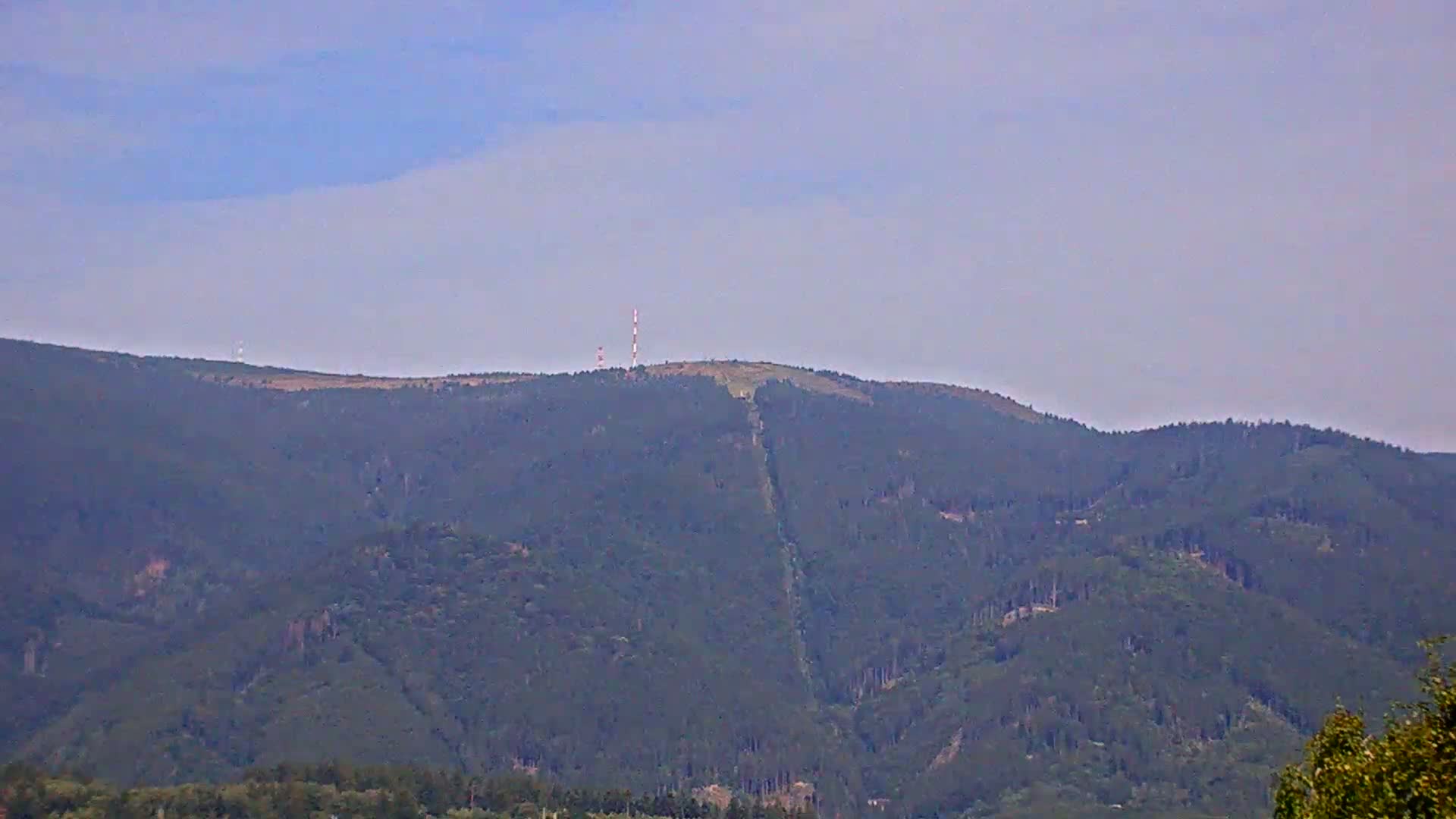 A distant view shows a mountain range under a hazy sky, with communication towers atop one peak.