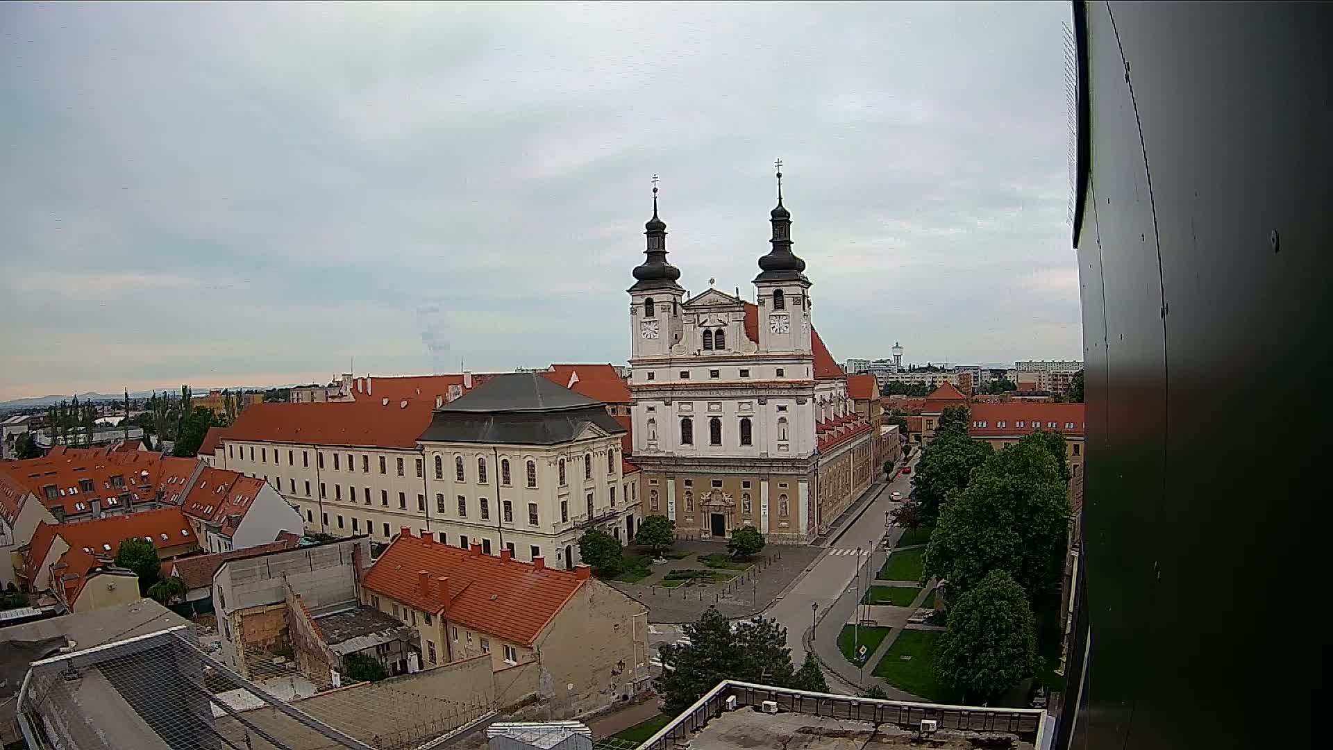 An elevated view shows a large, light-colored church with two towers in a city under an overcast sky.