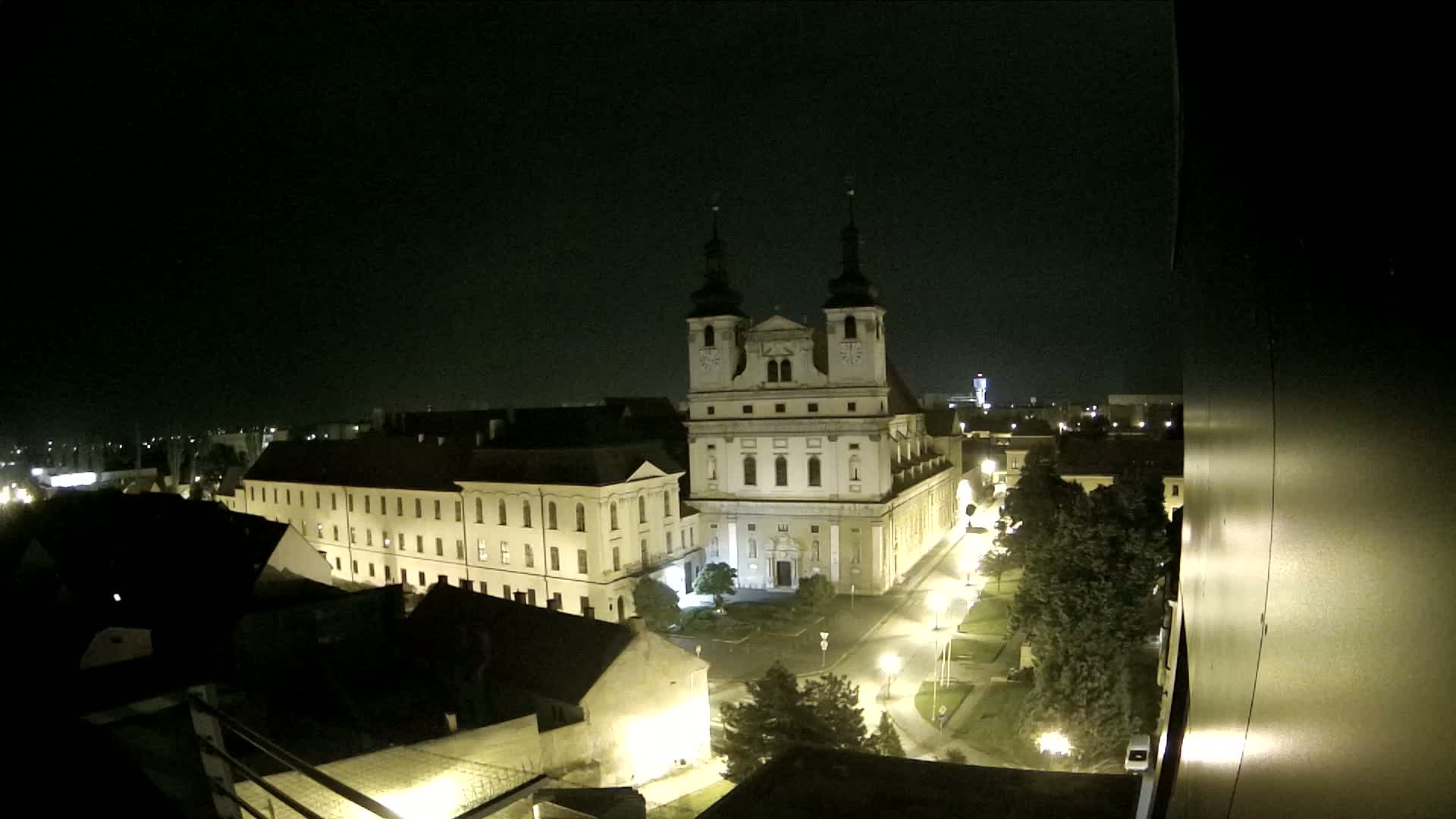 A nighttime, high-angle view shows a large church and surrounding buildings illuminated by streetlights, with a dark sky above.