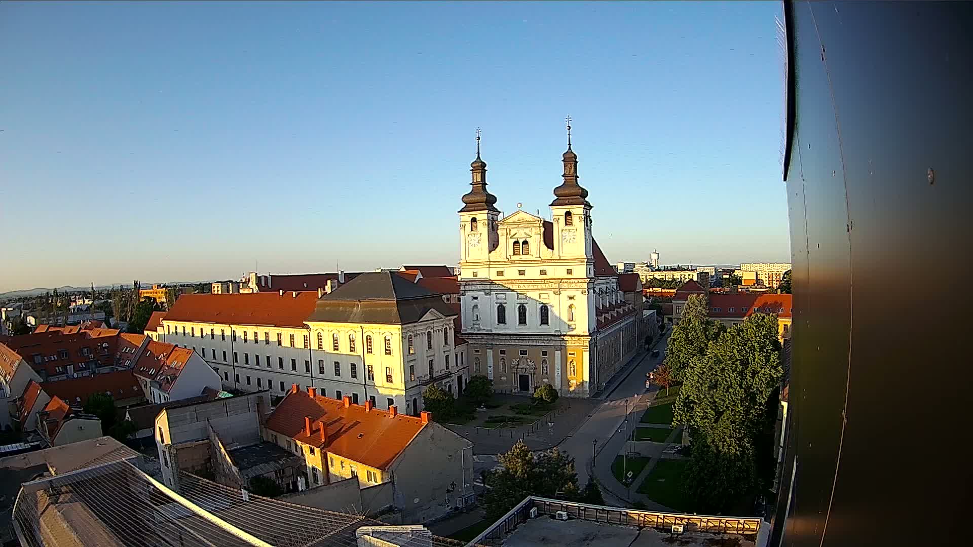 An elevated view shows a large church with two towers in a city under a clear, sunny sky.