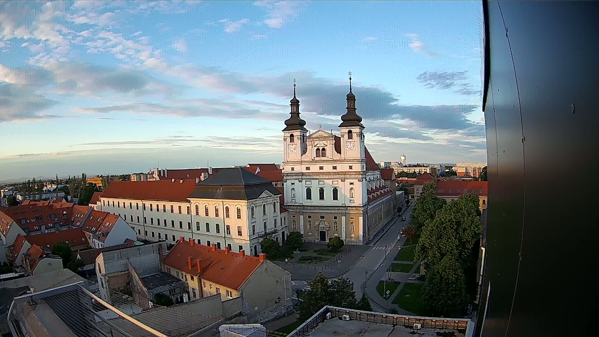 An elevated view of a city on a partly cloudy day, centered on a large church with two towers and surrounded by other buildings.
