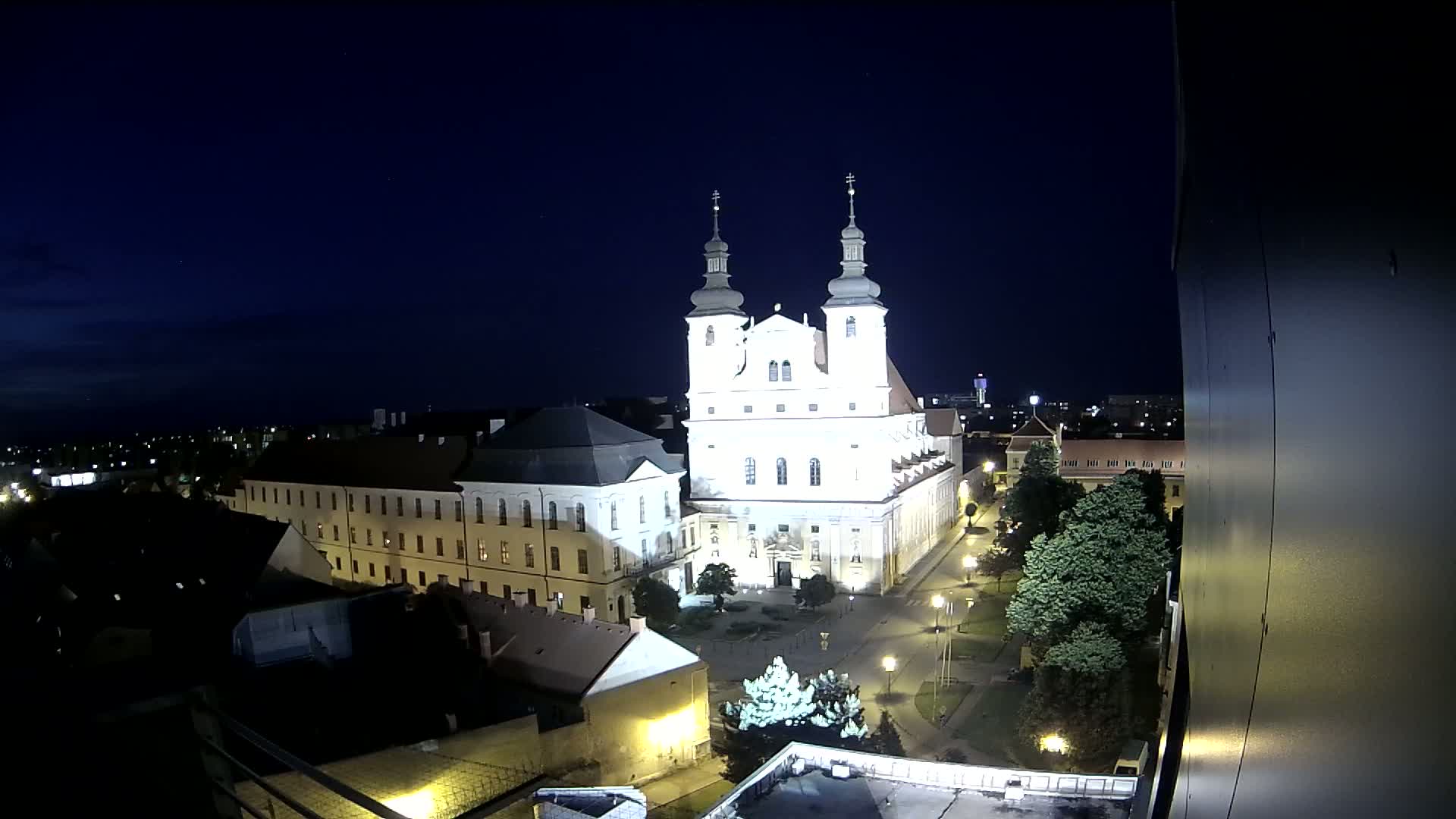 A brightly lit church and surrounding buildings are visible at night under a clear, dark sky.