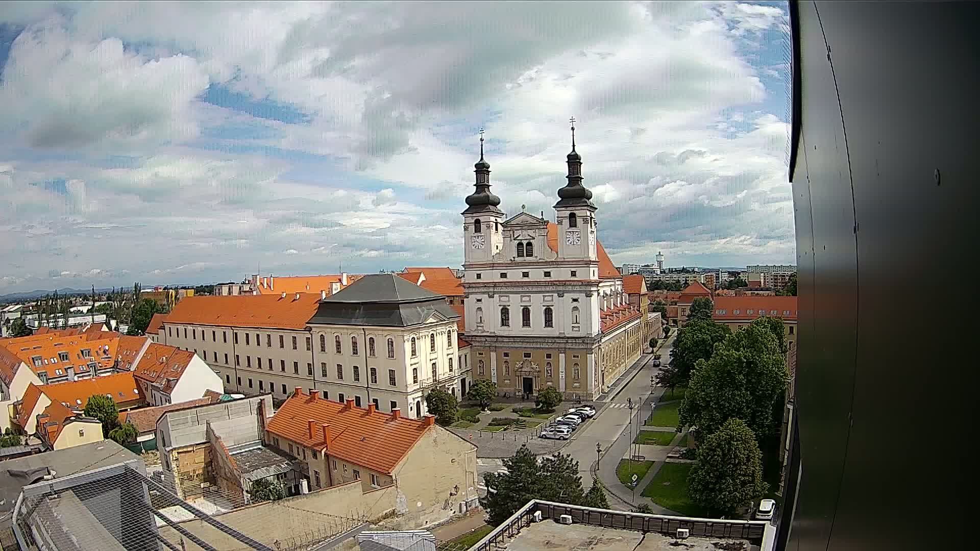 A large, light-colored church with two towers dominates a cityscape of red-tiled buildings under a partly cloudy sky.