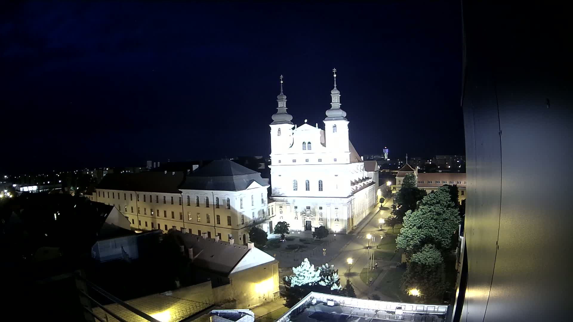 A brightly lit cathedral and surrounding buildings are visible at night, under a clear, dark sky.