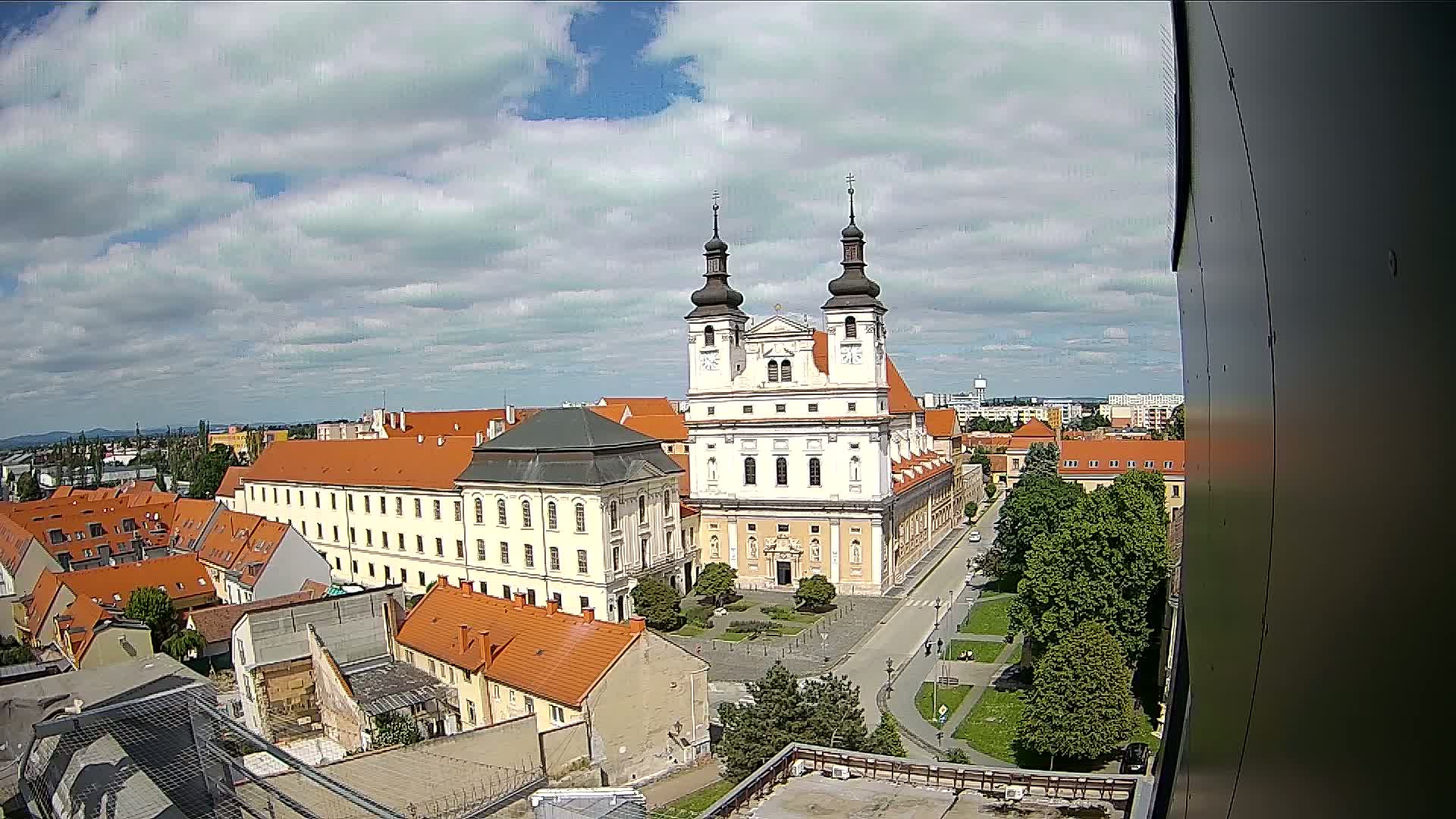 A large white church with twin towers stands in the center of a town under a partly cloudy sky.