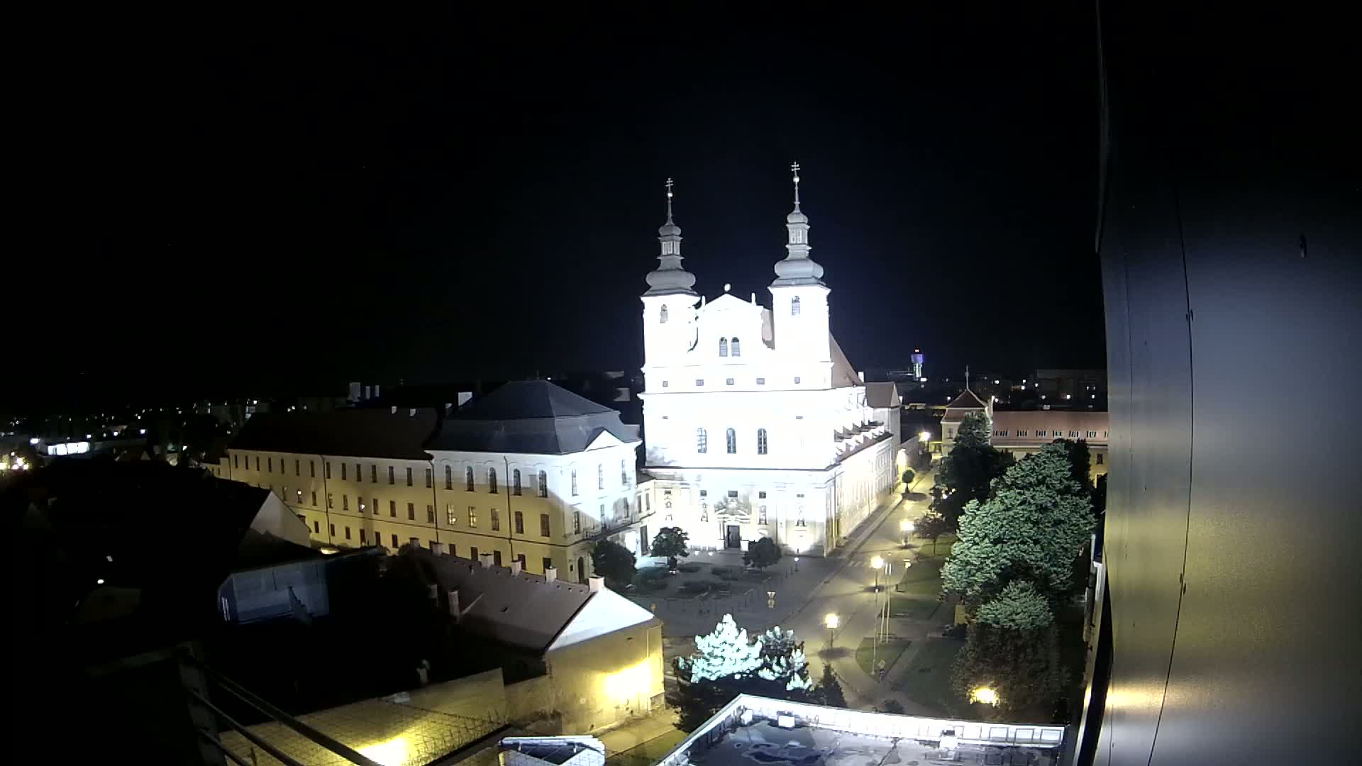 A brightly lit church and surrounding buildings are visible at night, under a clear, dark sky.