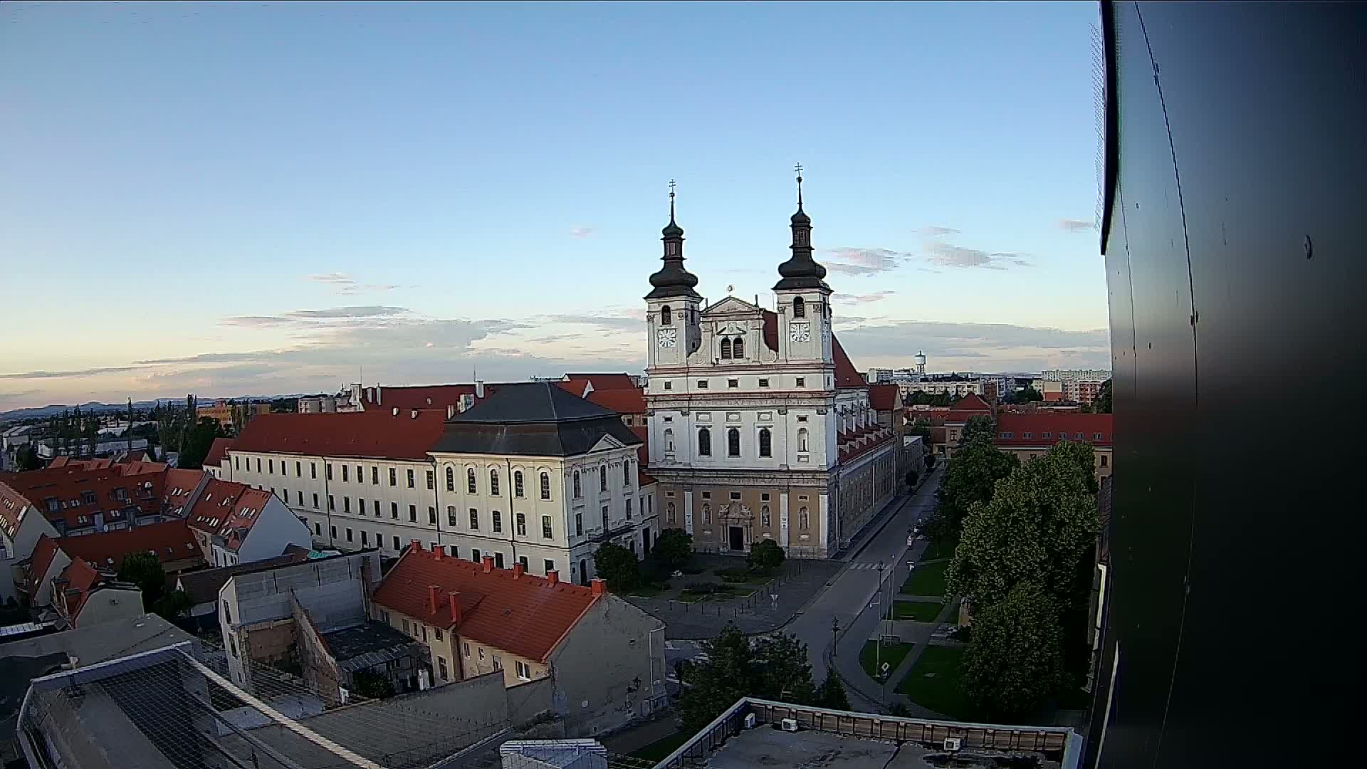An elevated view of a town square featuring a large white church with twin towers under a clear, twilight sky.