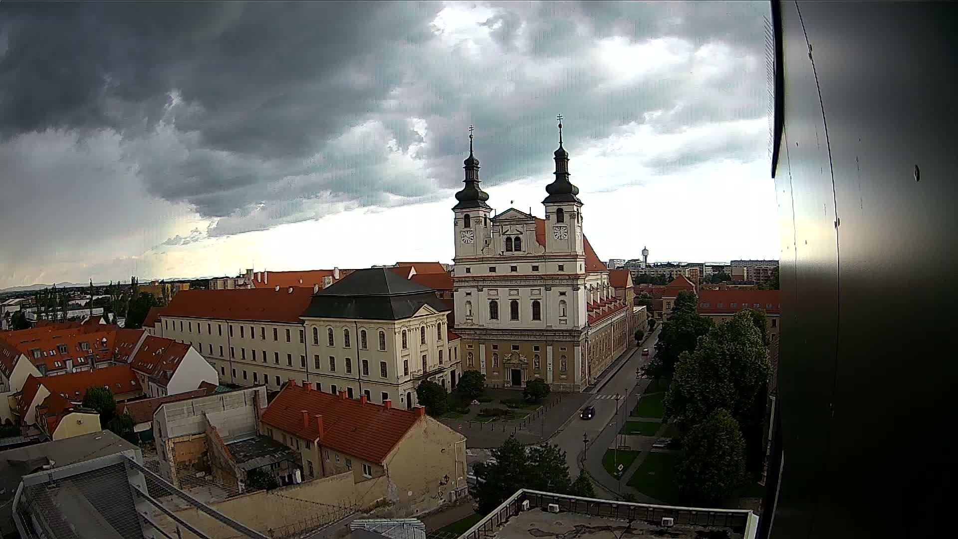 An aerial view of a city under a dark, cloudy sky shows a large church and surrounding buildings.