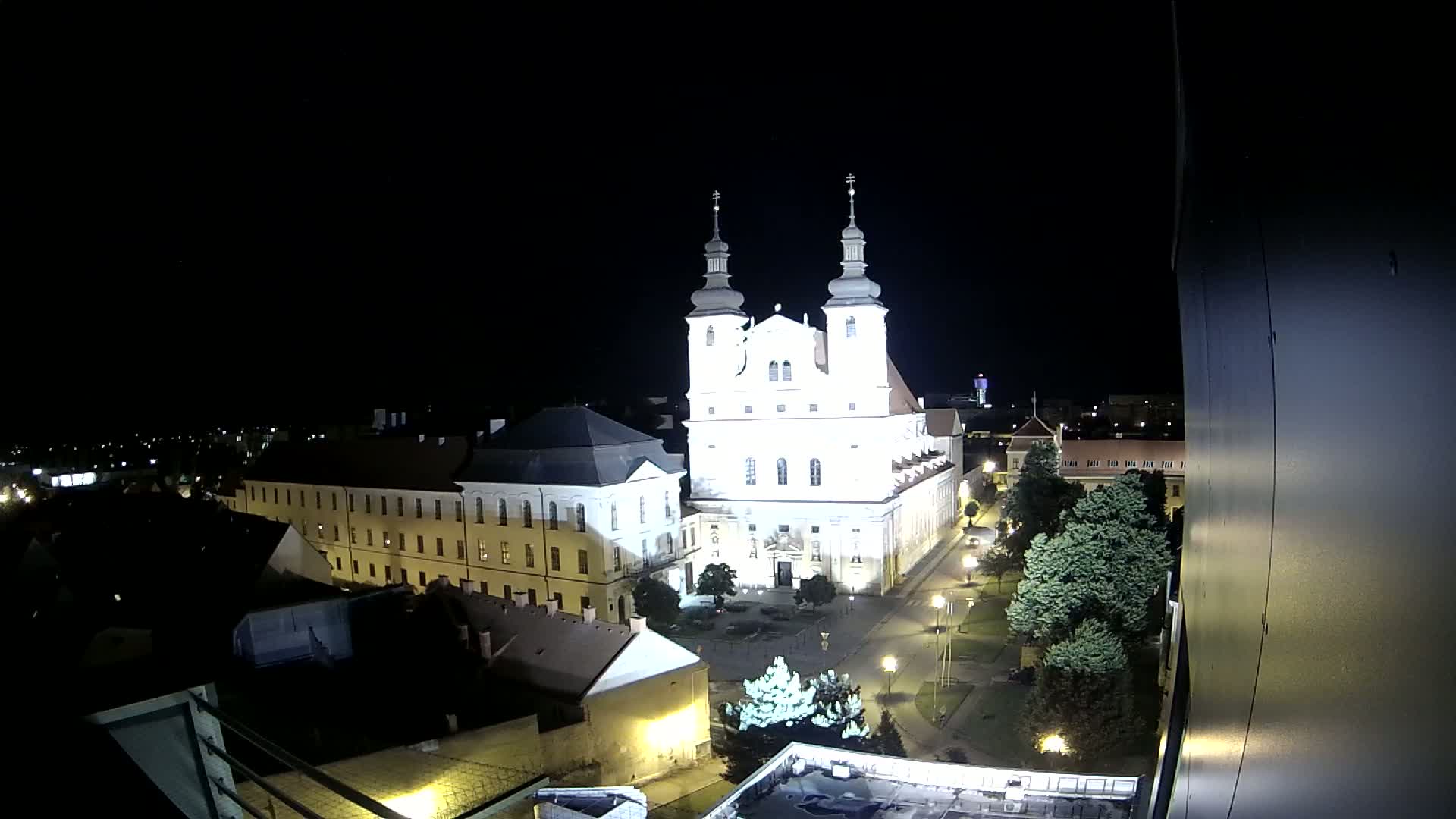 A brightly lit church and surrounding buildings are visible at night, viewed from an elevated position.