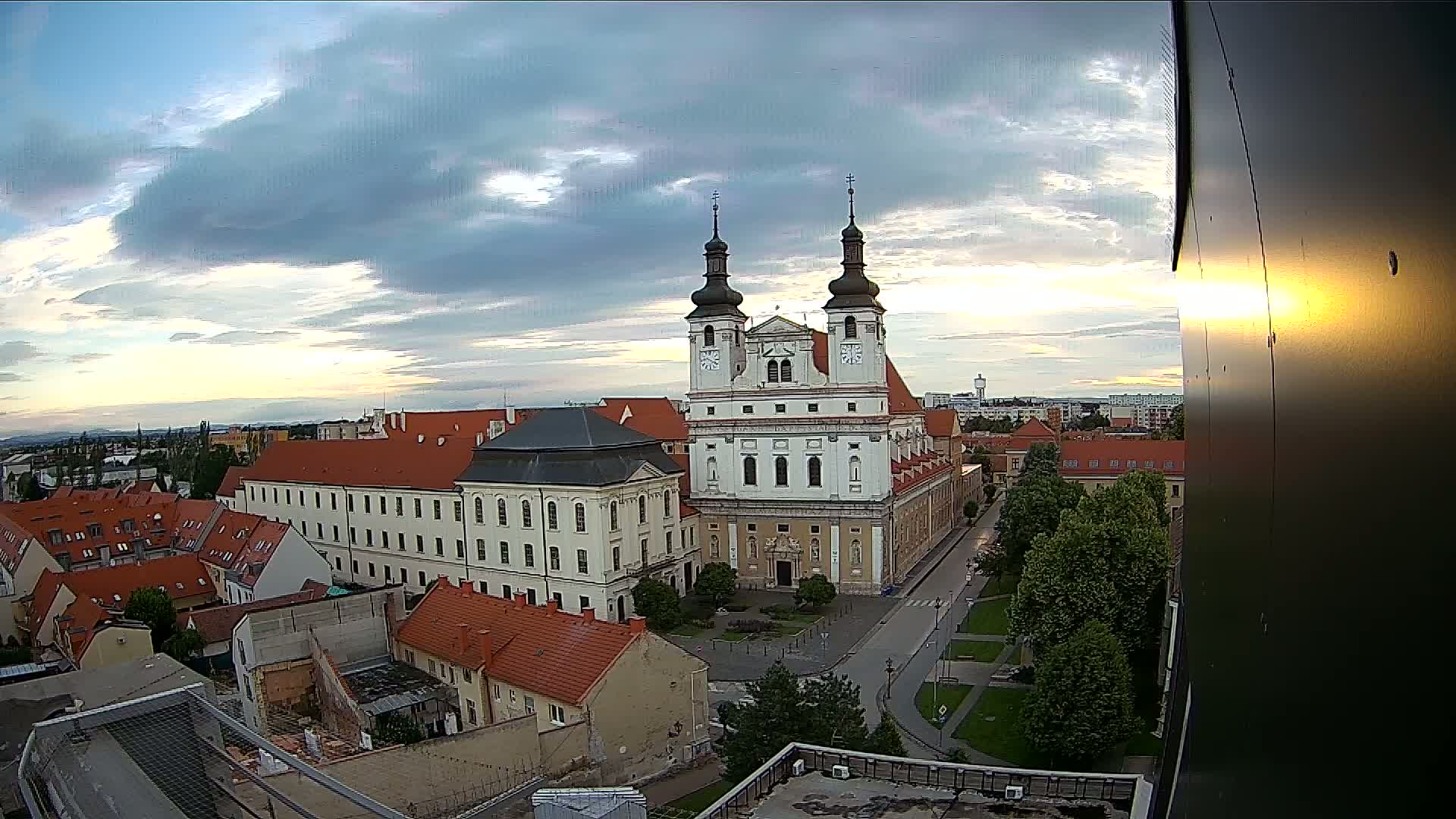 An elevated view of a town square with a large church at sunset under partly cloudy skies.