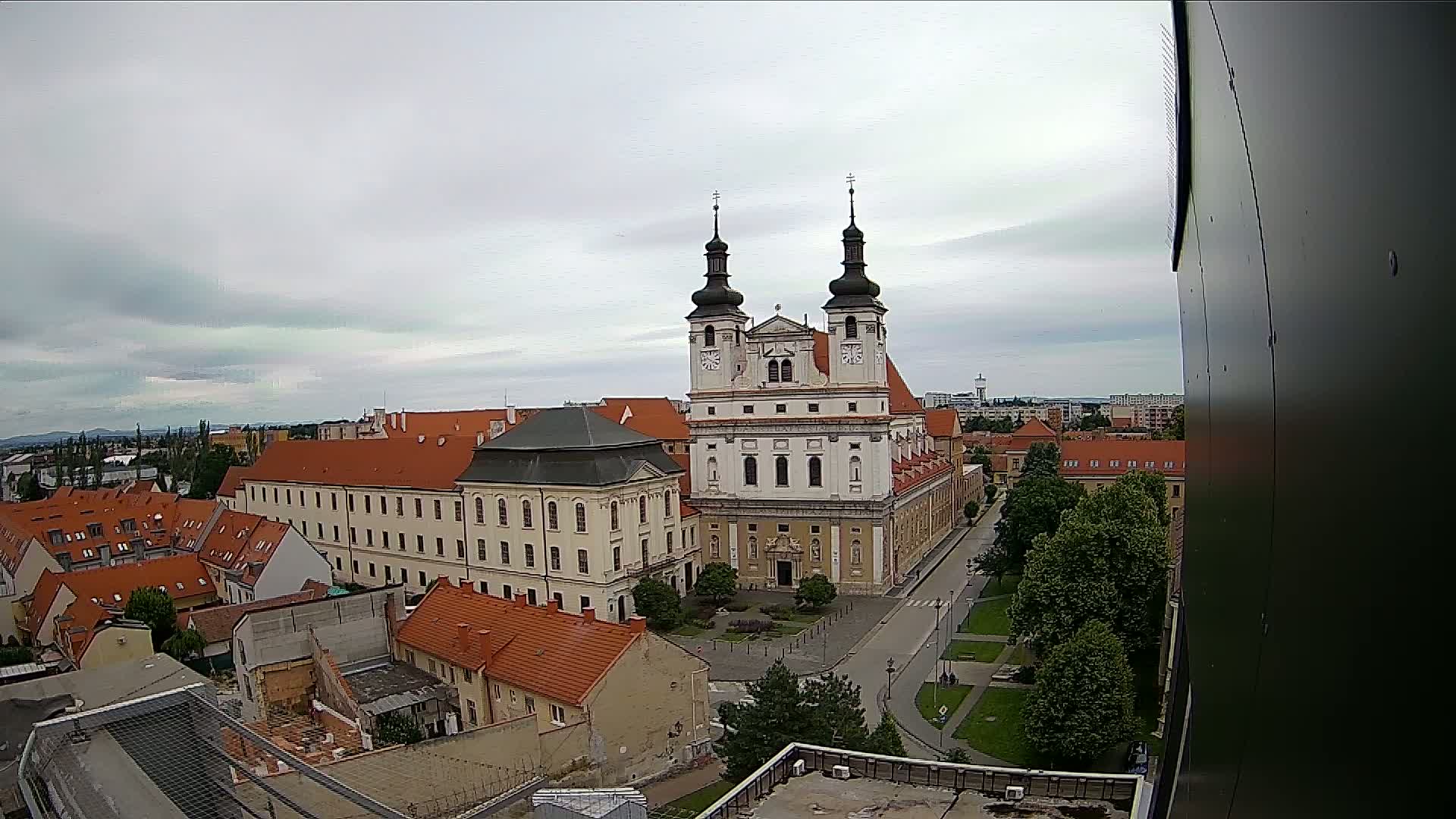 An elevated view shows a large, light-colored church with two towers in a city under an overcast sky.