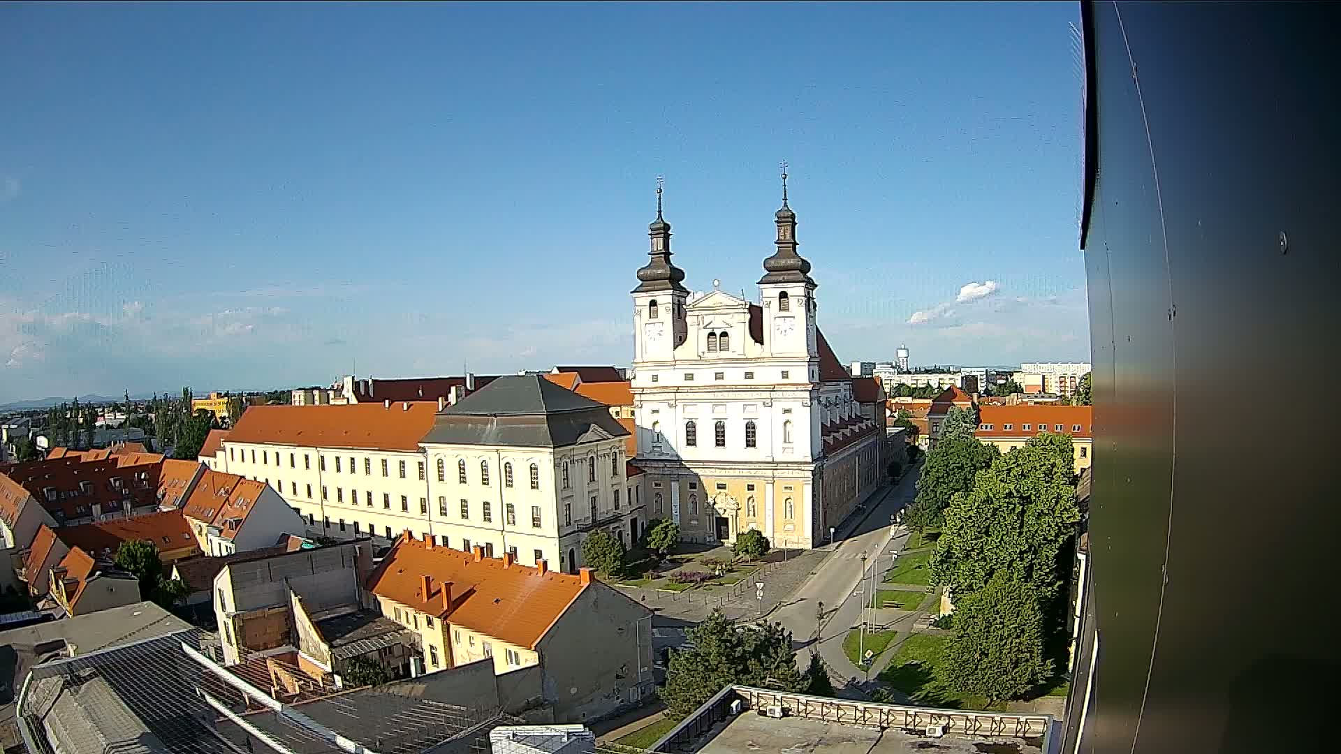 A large white church with twin towers stands in a city square surrounded by low-rise buildings under a mostly clear blue sky.