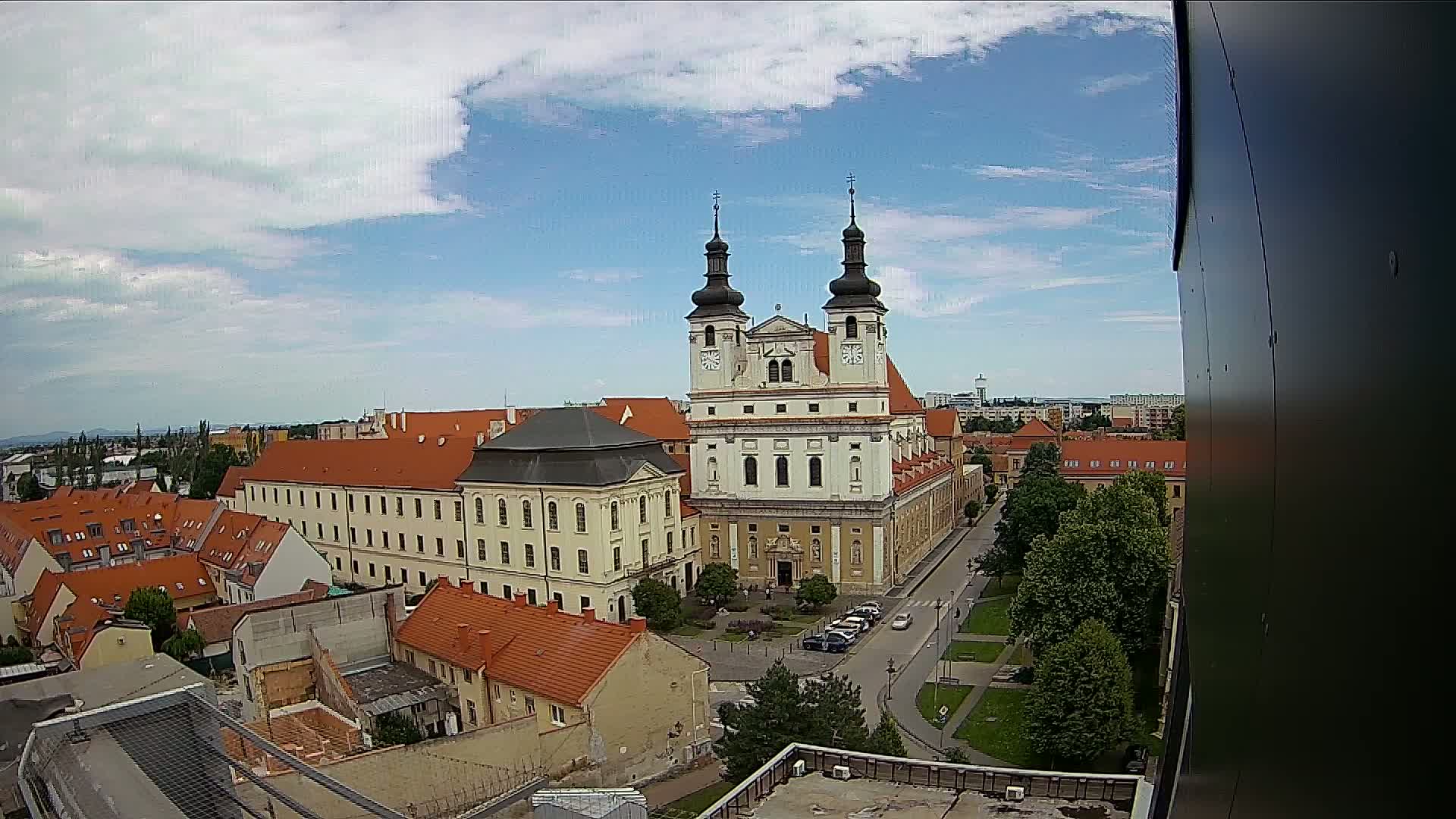 A large, light-colored church with two towers is the central feature of a city view on a partly cloudy day.
