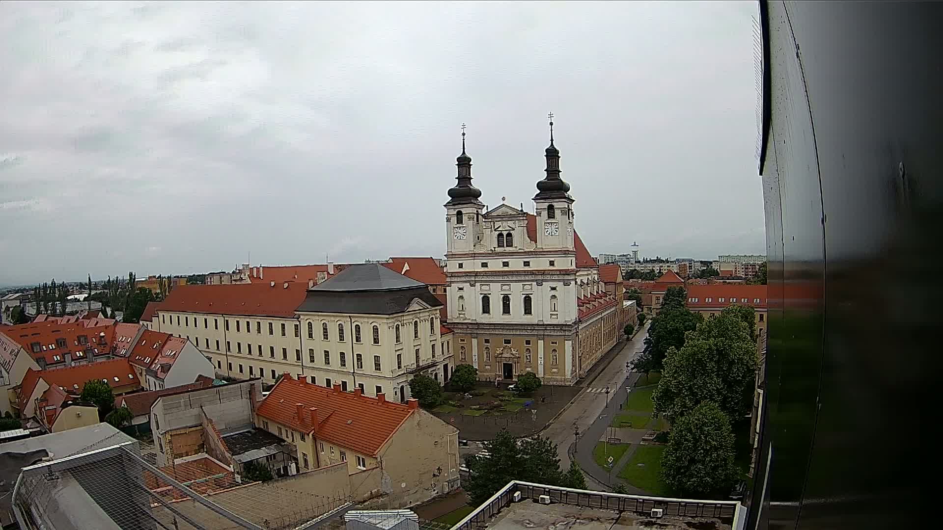 A large church with two towers is the central feature of an overcast city vista, surrounded by low buildings and green spaces.