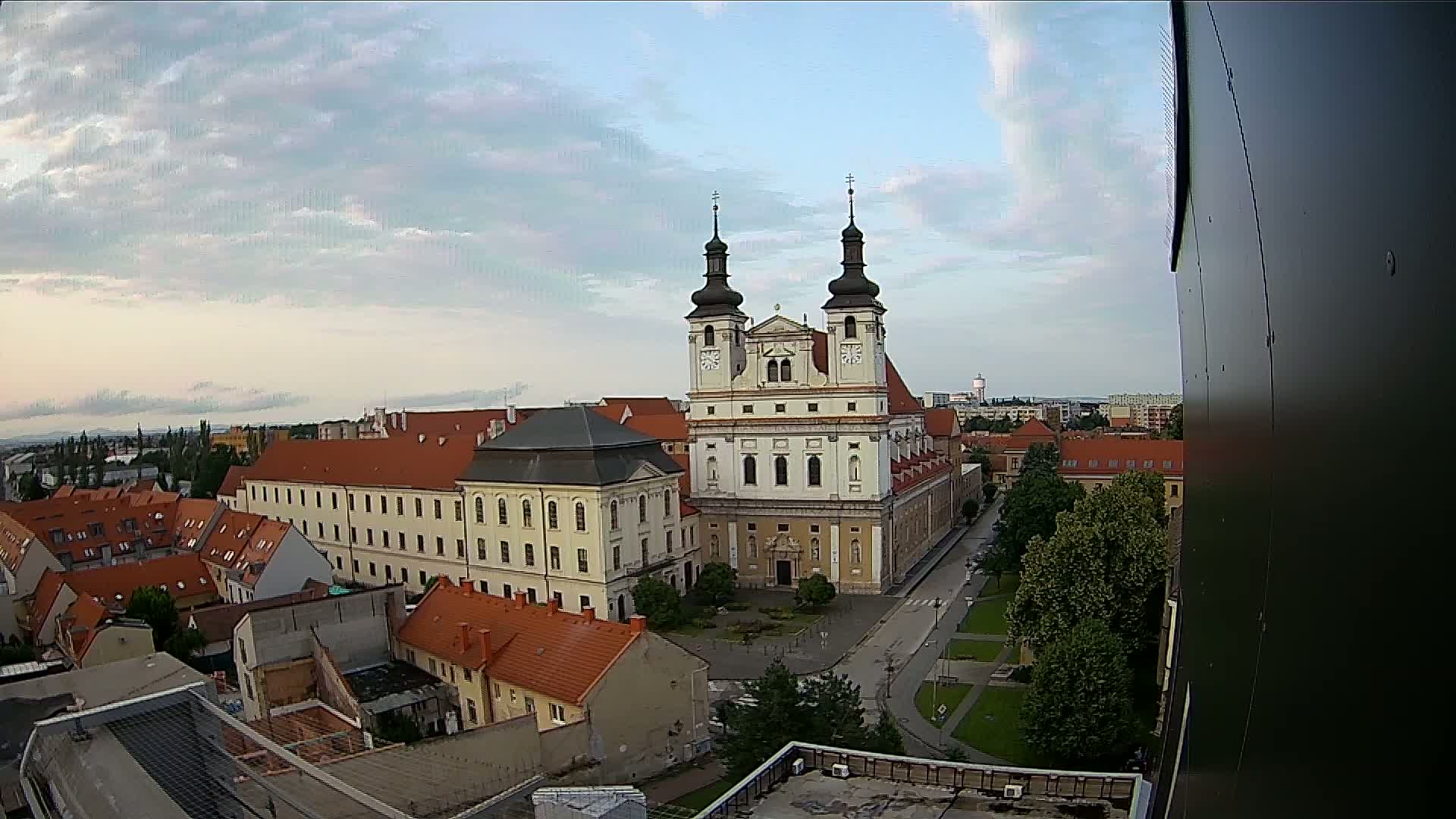 A large church with two towers stands in a city under a partly cloudy sky.