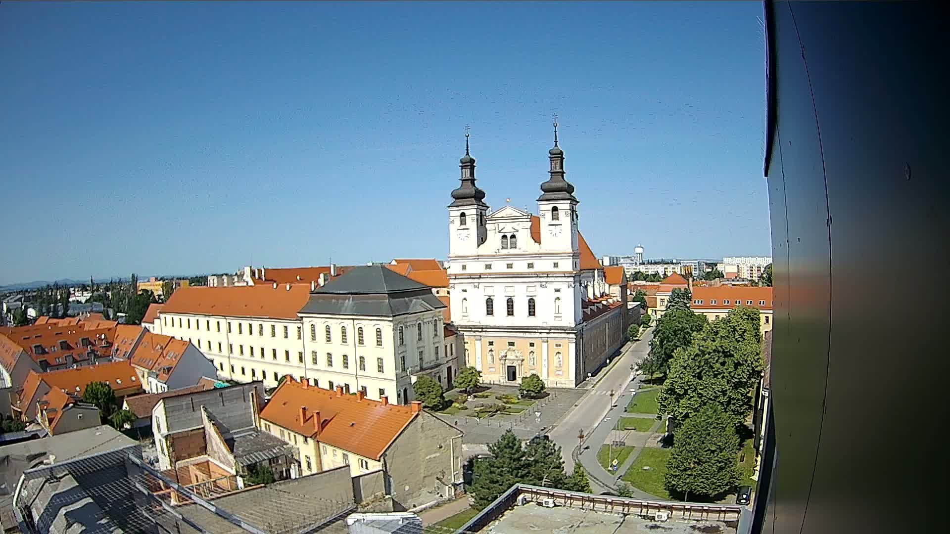 A large, light-colored church with twin towers stands in the center of a town under a clear blue sky.