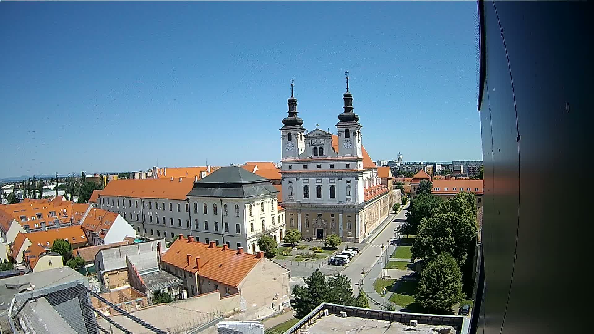 A large church with twin towers stands prominently in a city square, surrounded by low-rise buildings under a clear, sunny sky.