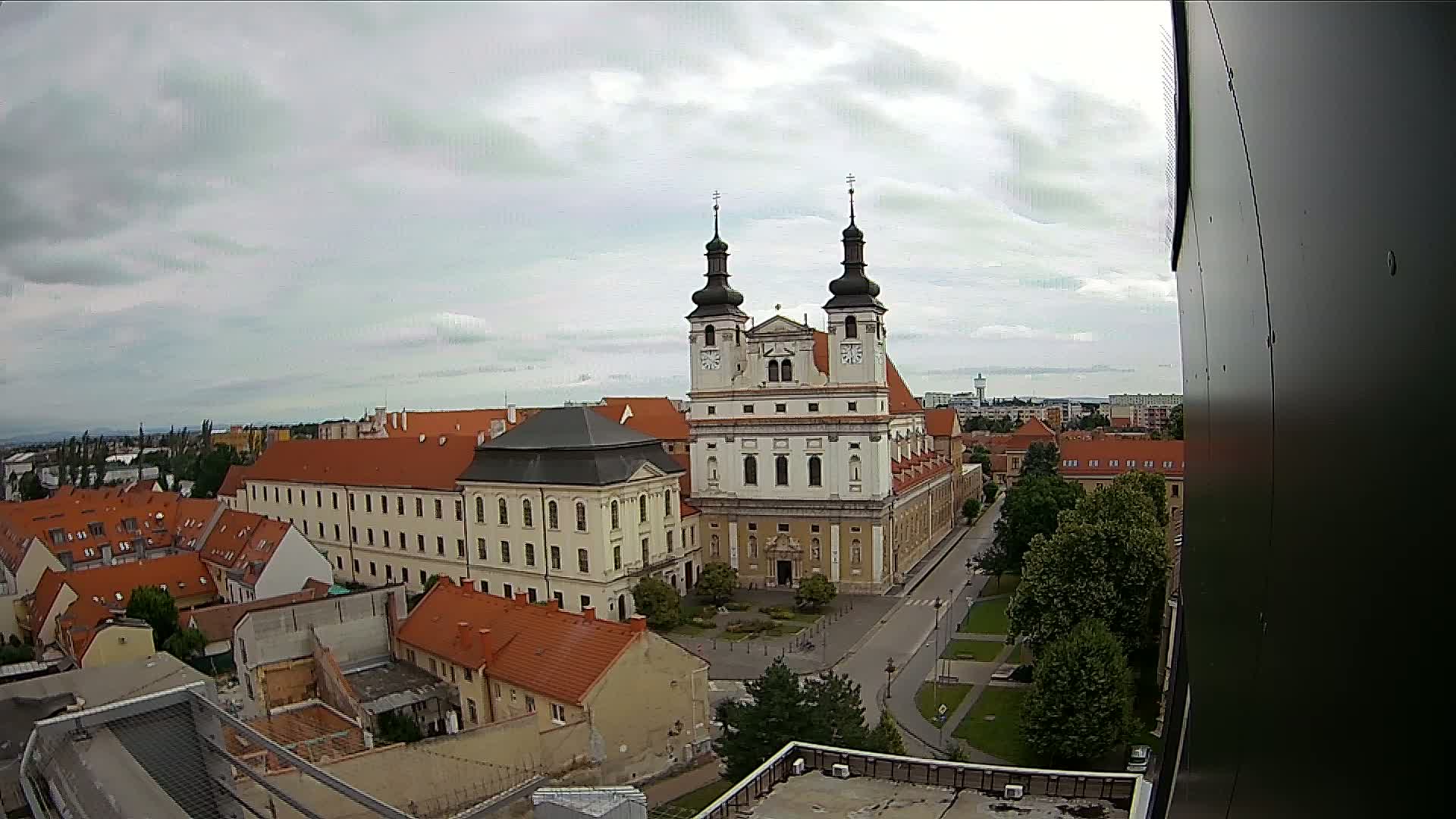 A large white church with two dark towers stands prominently in a city under a cloudy sky.