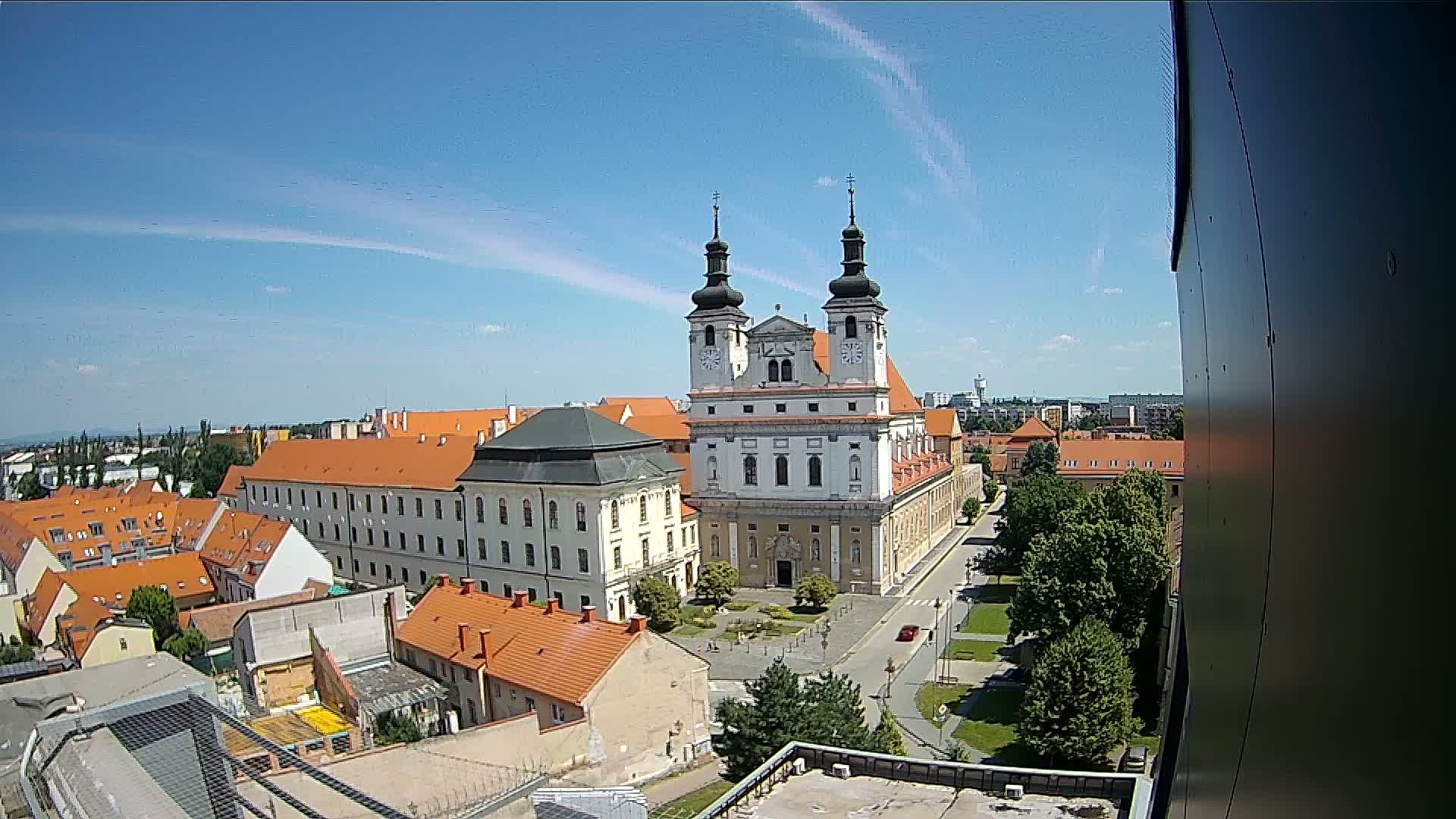 A large white church with twin towers stands in the center of a town under a mostly sunny sky with a few wispy clouds.