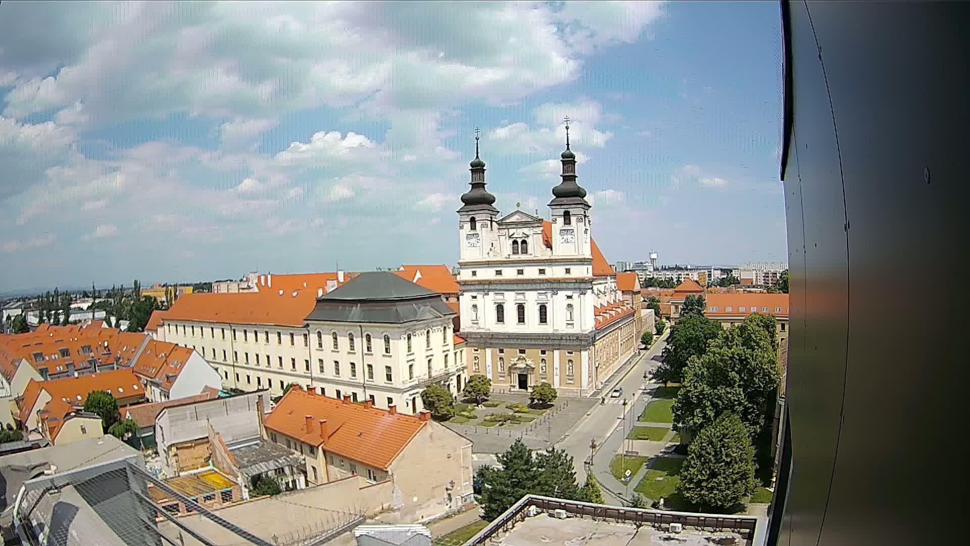 A large church with two towers stands in the center of a town under a partly cloudy sky.