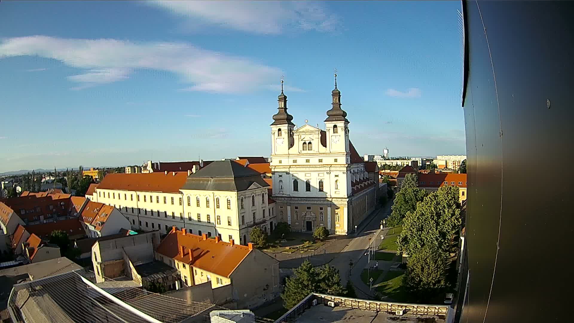 A large, light-colored church with twin towers is the central feature of an aerial view of a city under a mostly clear, sunny sky.