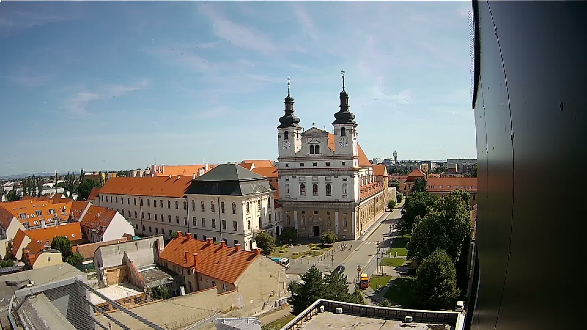 A large, light-colored church with twin towers is the central feature of an aerial view of a city under a mostly clear, sunny sky.