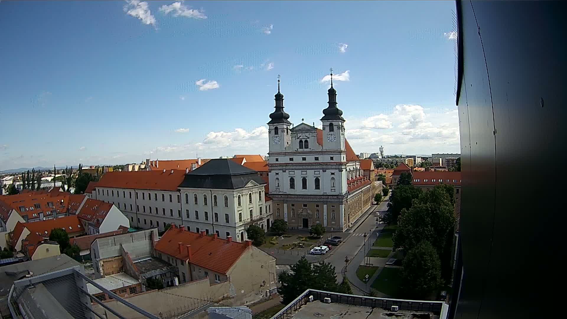 A large white church with two dark towers stands prominently in a city under a mostly sunny sky with some scattered clouds.