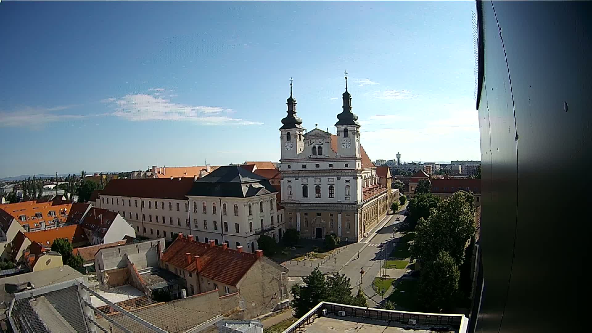 A large church with two towers stands in the center of a town under a mostly sunny sky.