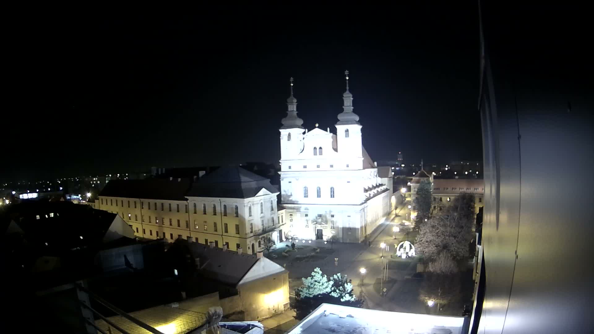 An illuminated white church with twin spires stands prominently in a clear, dark night cityscape, surrounded by other buildings and streets lit by streetlights.