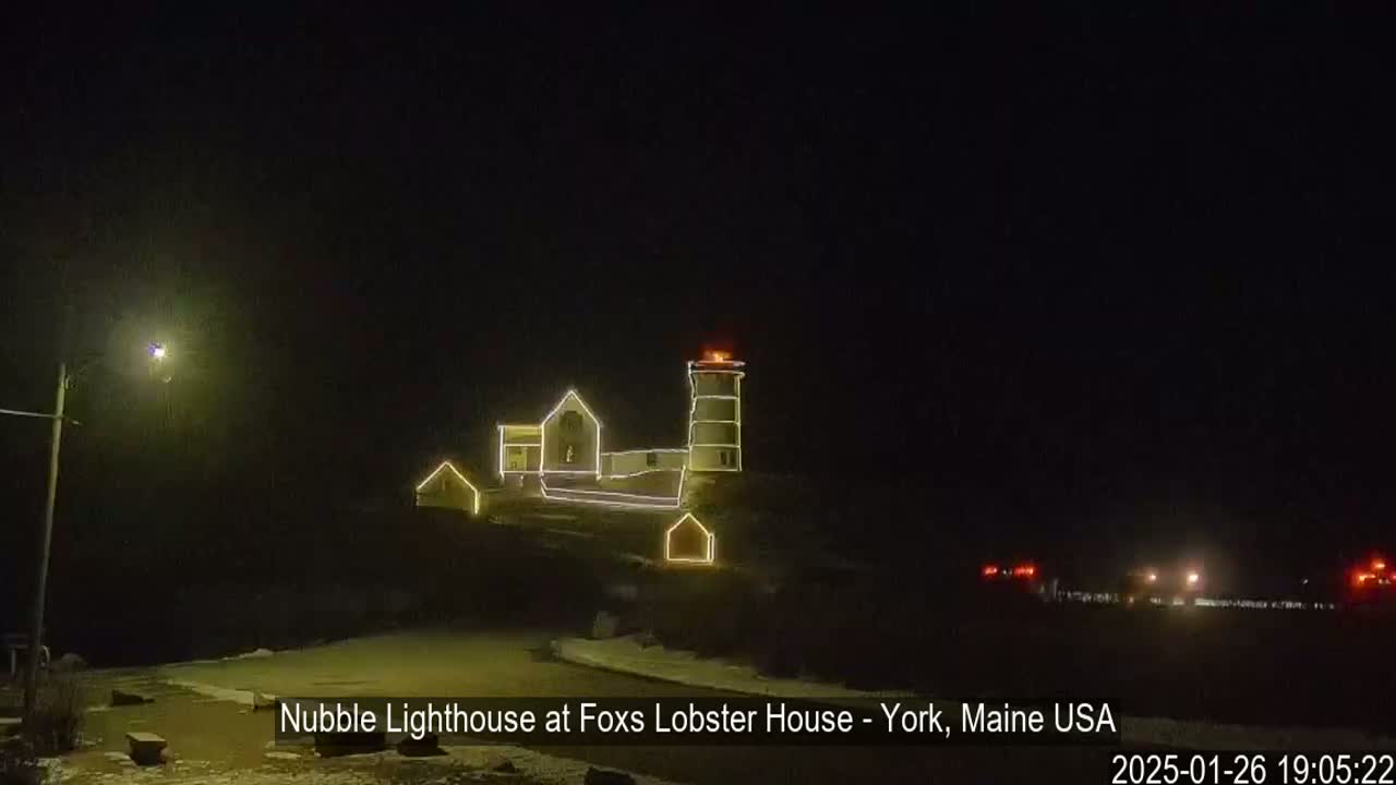 A lighthouse and adjacent buildings are illuminated at night with string lights, under a dark, clear sky.